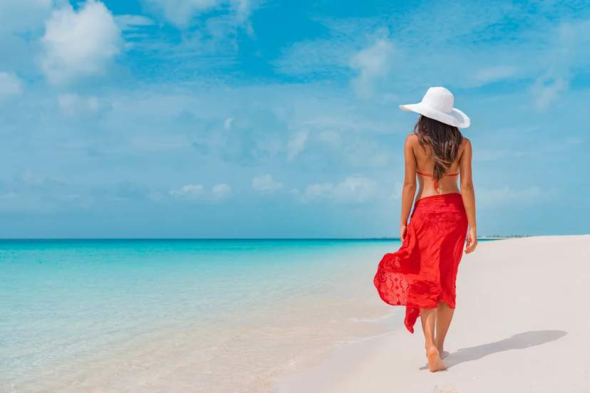 Mujer camina en playa de arena blanca y mar turquesa, rodeada de paz y belleza natural.