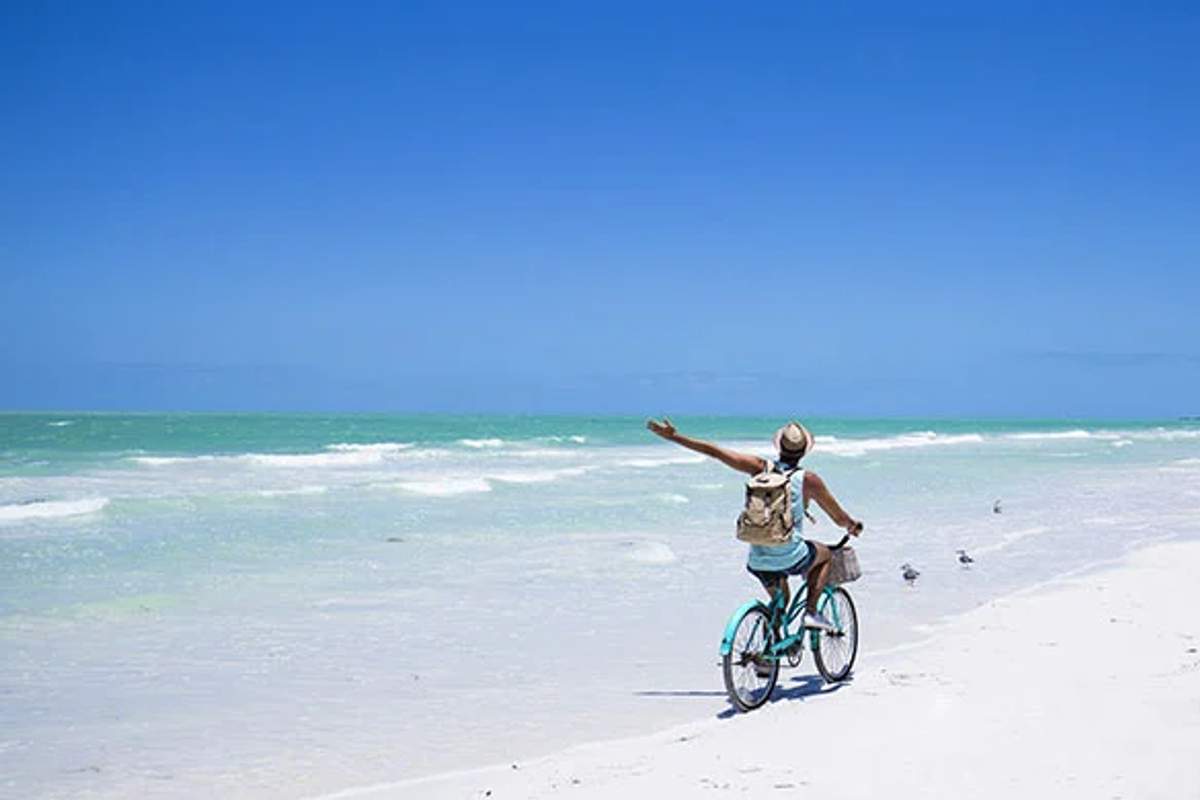 Un ciclista disfruta de un paseo por la playa de arena blanca de Holbox bajo un cielo azul claro.