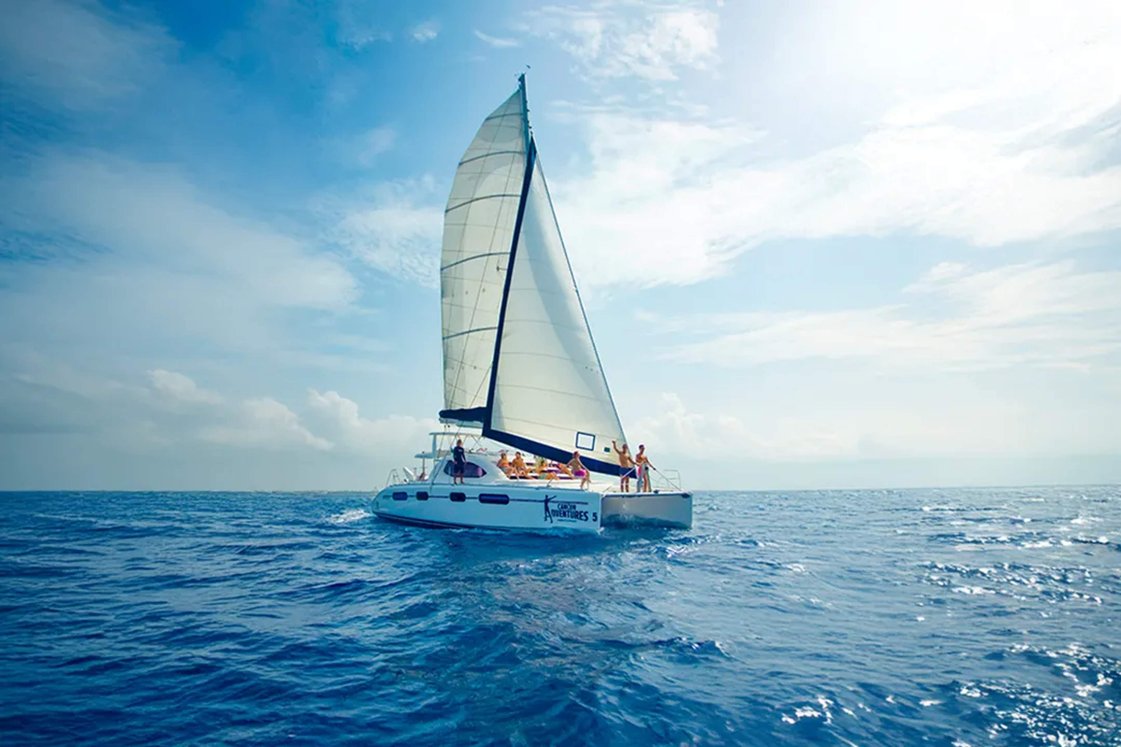 Luxury catamaran sailing tour in Cancun with guests onboard cruising turquoise Caribbean waters under clear sky