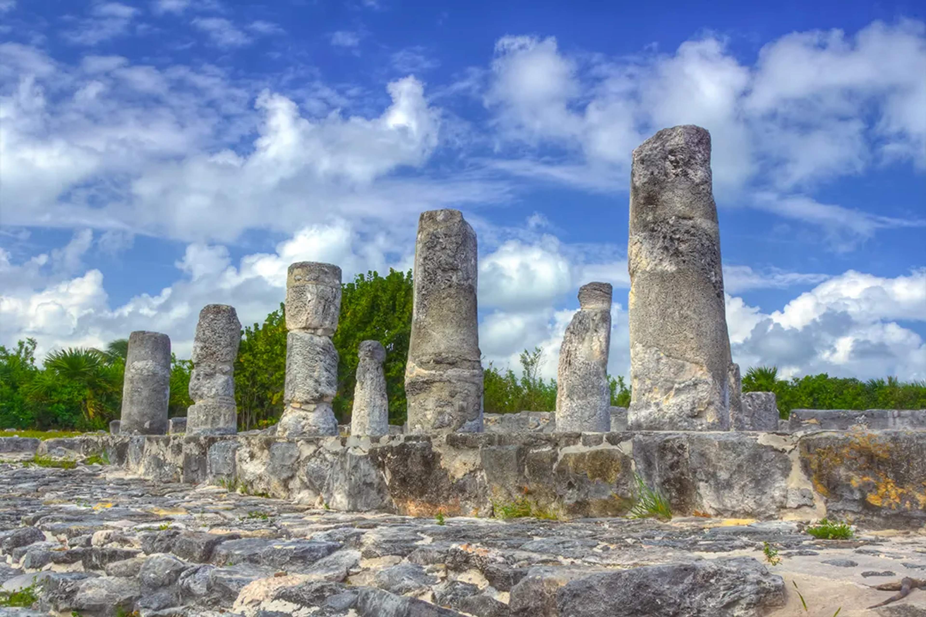Stone columns of El Rey ruins stand under a bright sky, surrounded by lush tropical greenery.