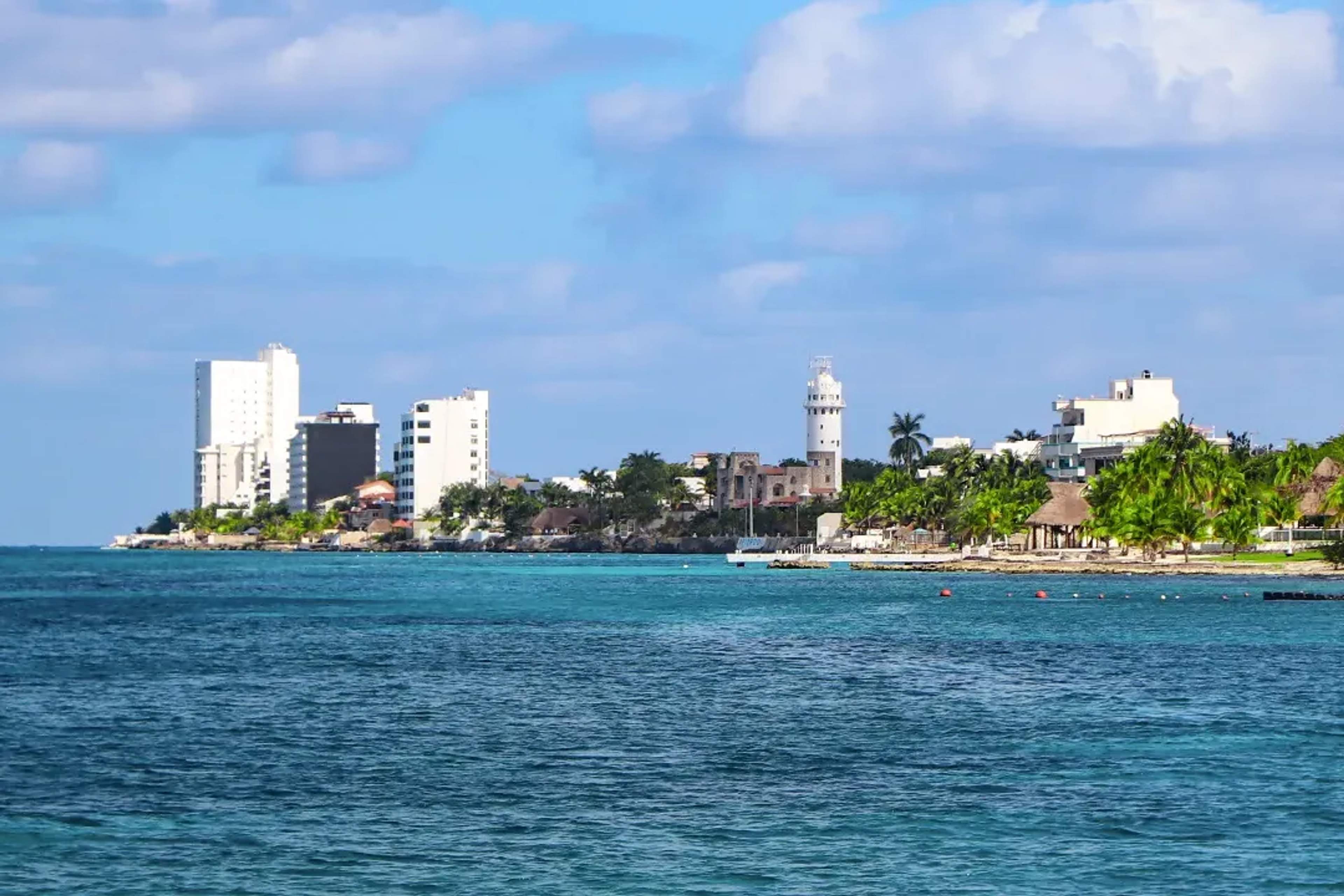 Vista costera de Cozumel con edificios modernos, palmeras y aguas cristalinas, ideal para disfrutar del Caribe.