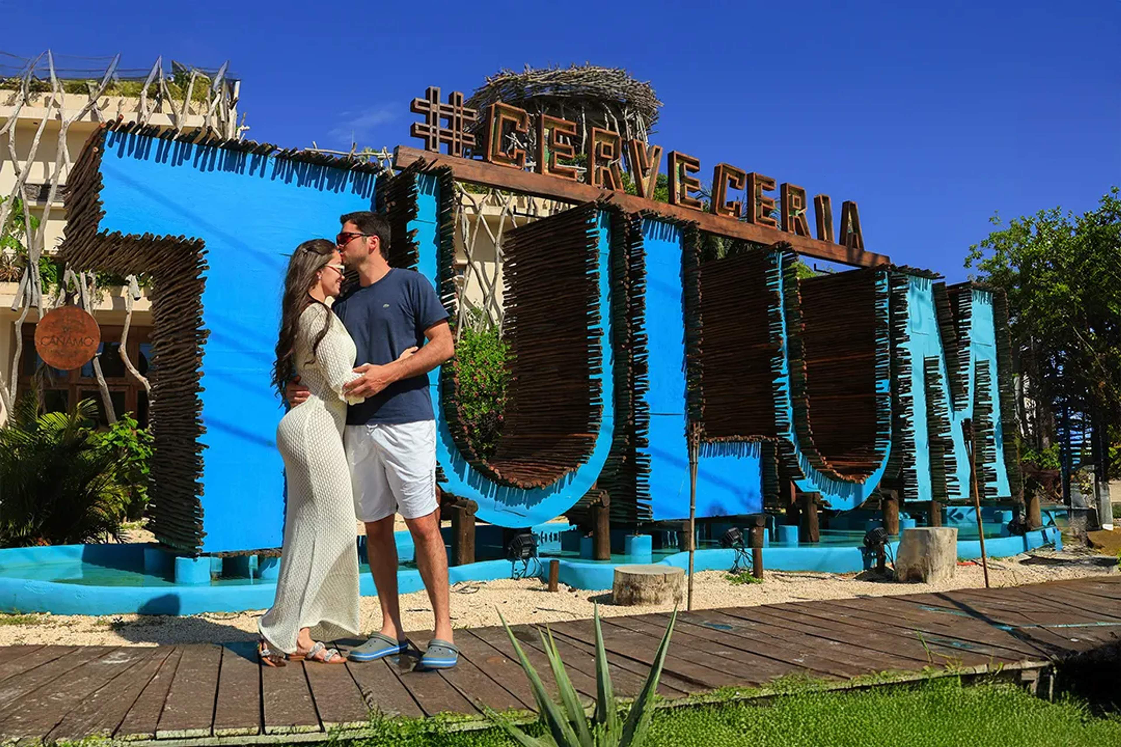 Couple posing for a romantic photo in front of the iconic blue Tulum sign, a popular spot during the Insta Tulum Tour