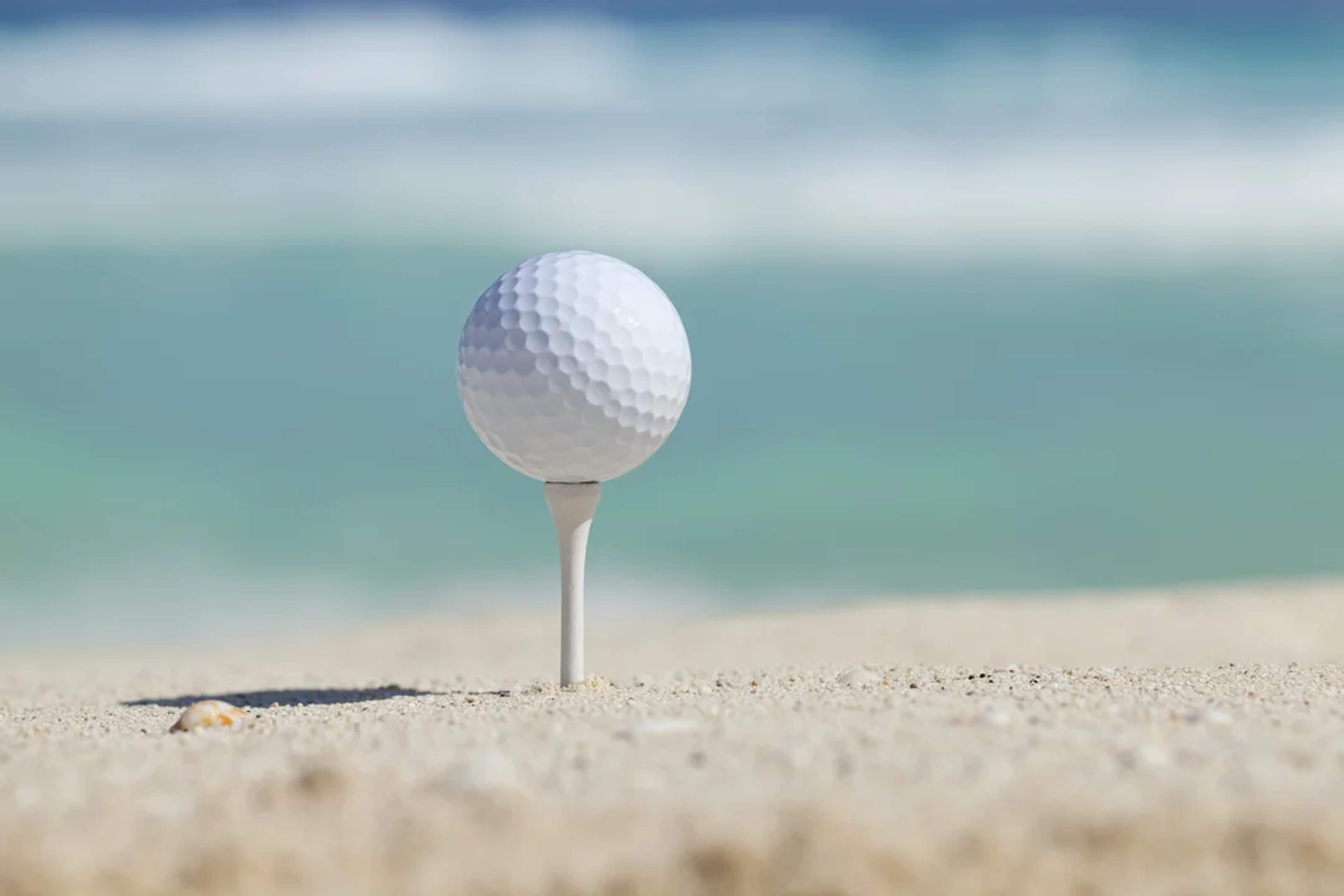 Pelota de golf sobre la arena con el mar Caribe al fondo, ideal para golf en la playa.