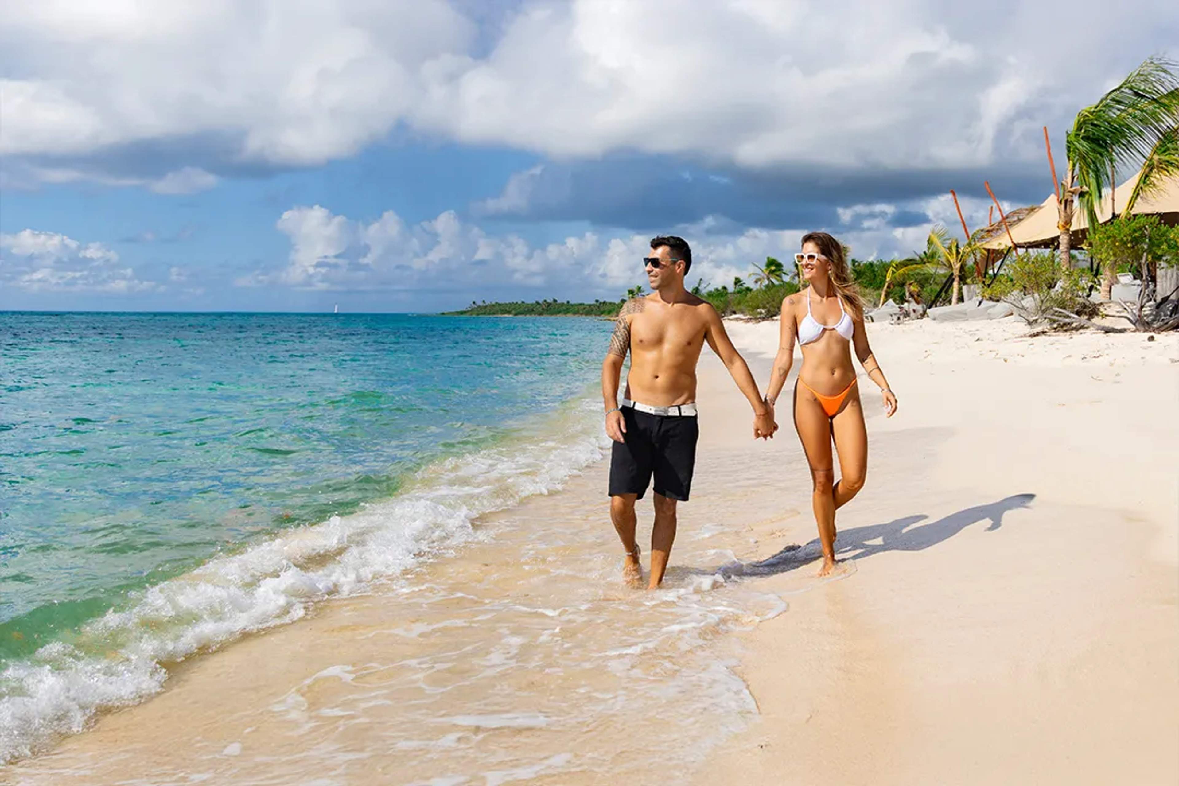 Pareja caminando en playa de arena blanca durante tour de catamarán y snorkel en Riviera Maya