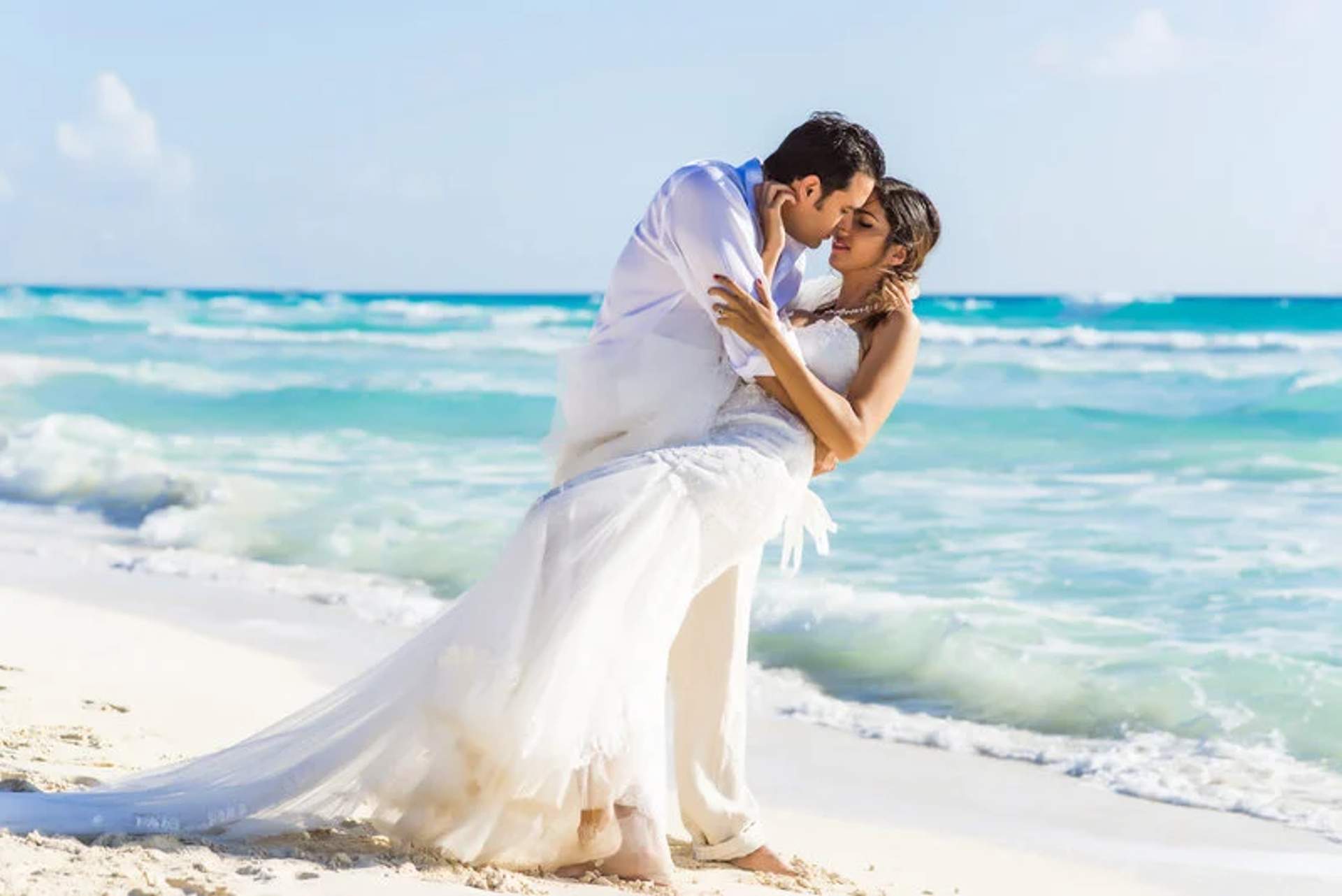 Una pareja comparte un momento romántico en su recepción de boda en la playa de Punta Venado en Cancún, con el océano turquesa como telón de fondo.