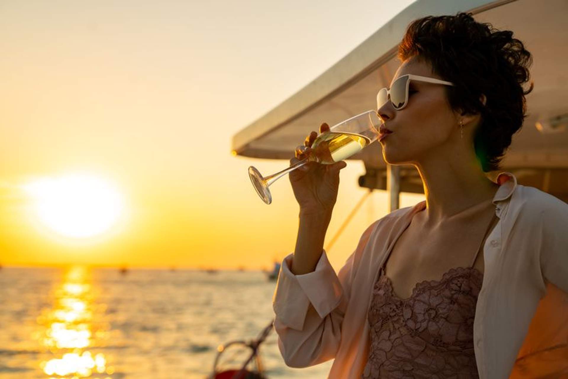 Woman drinking a glass of wine on a yacht during sunset. 
