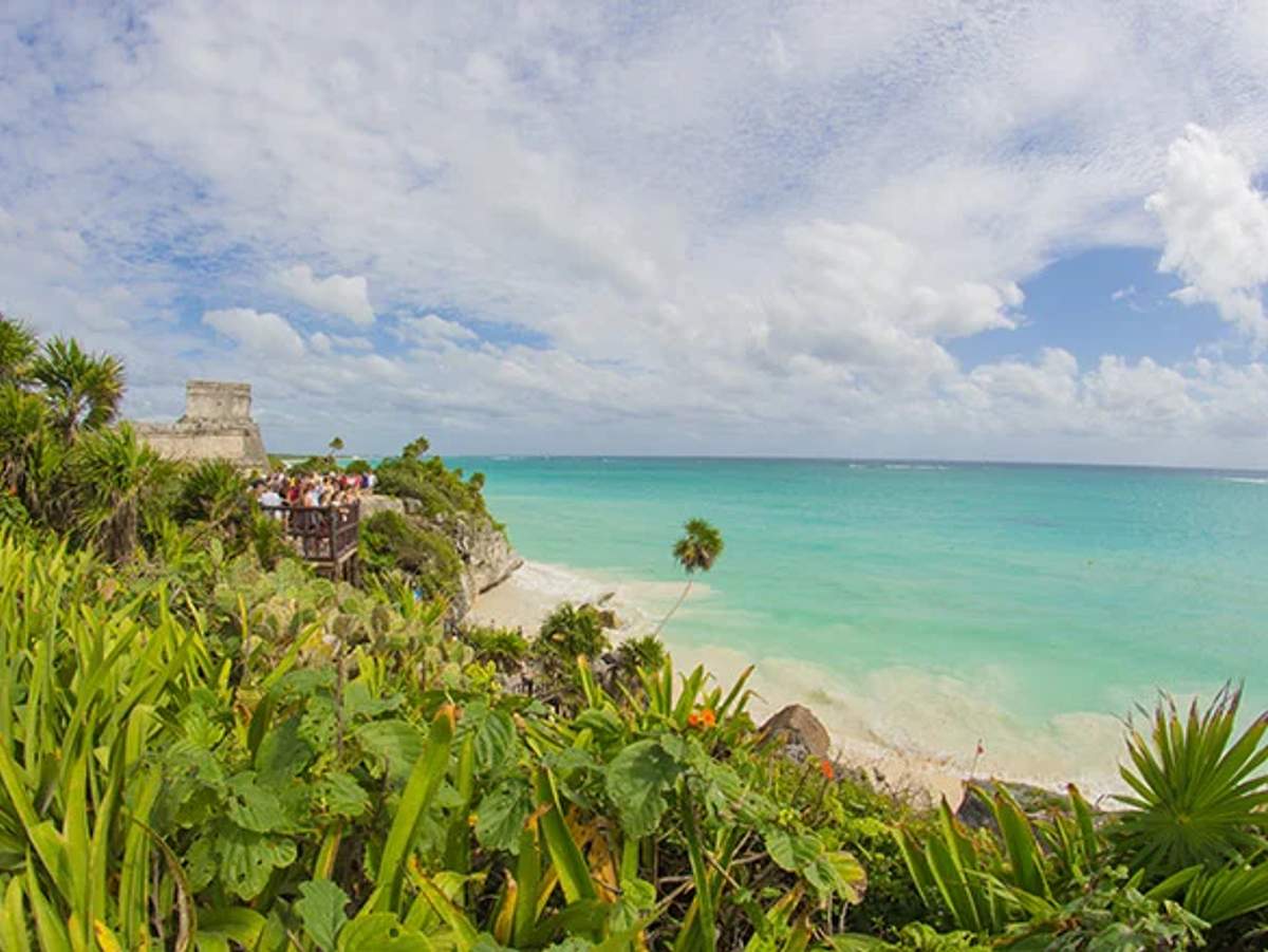 View of Tulum ruins overlooking a beautiful beach with turquoise waters and lush vegetation.