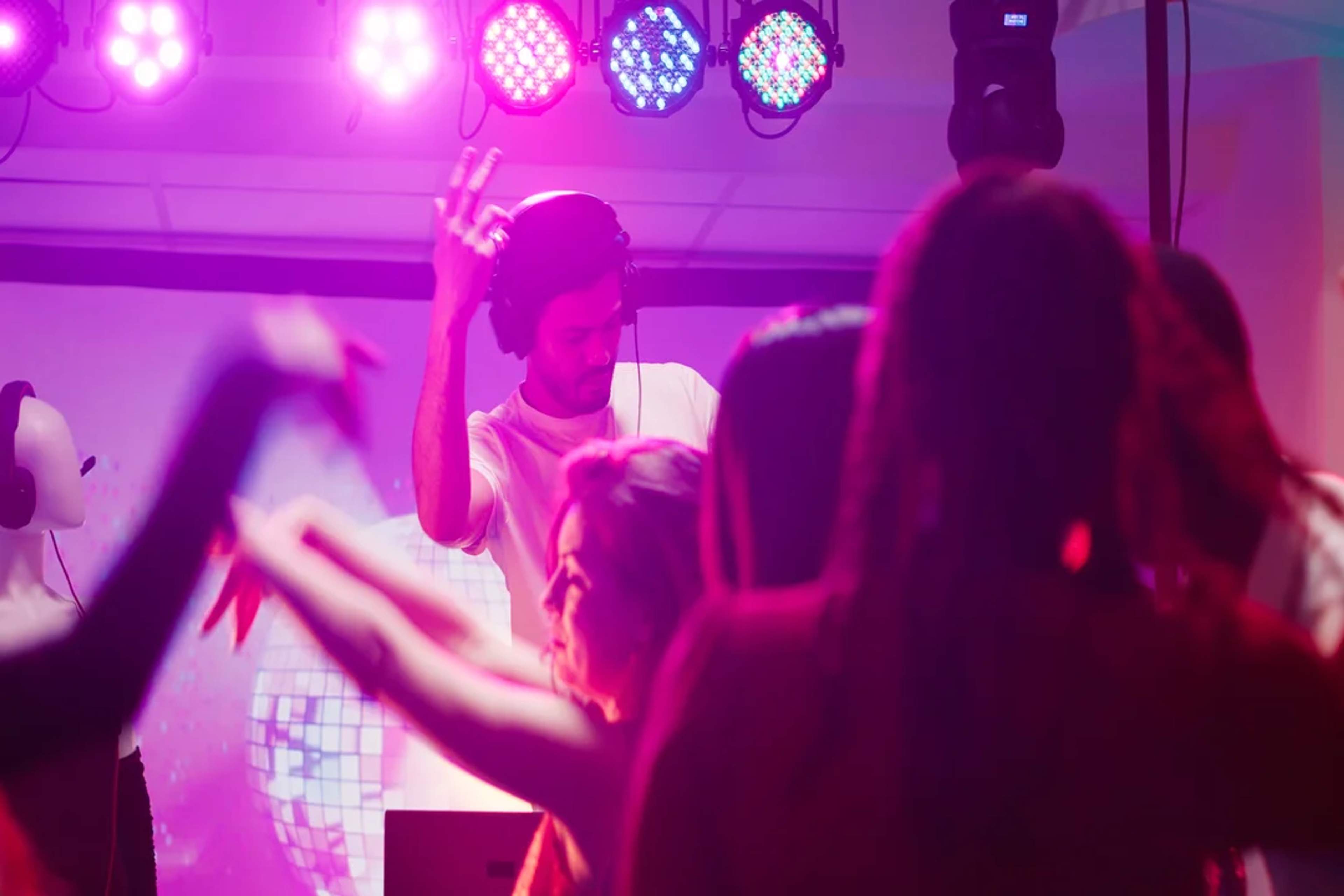 Escena animada de discoteca con un DJ tocando música mientras la gente baila bajo luces vibrantes.