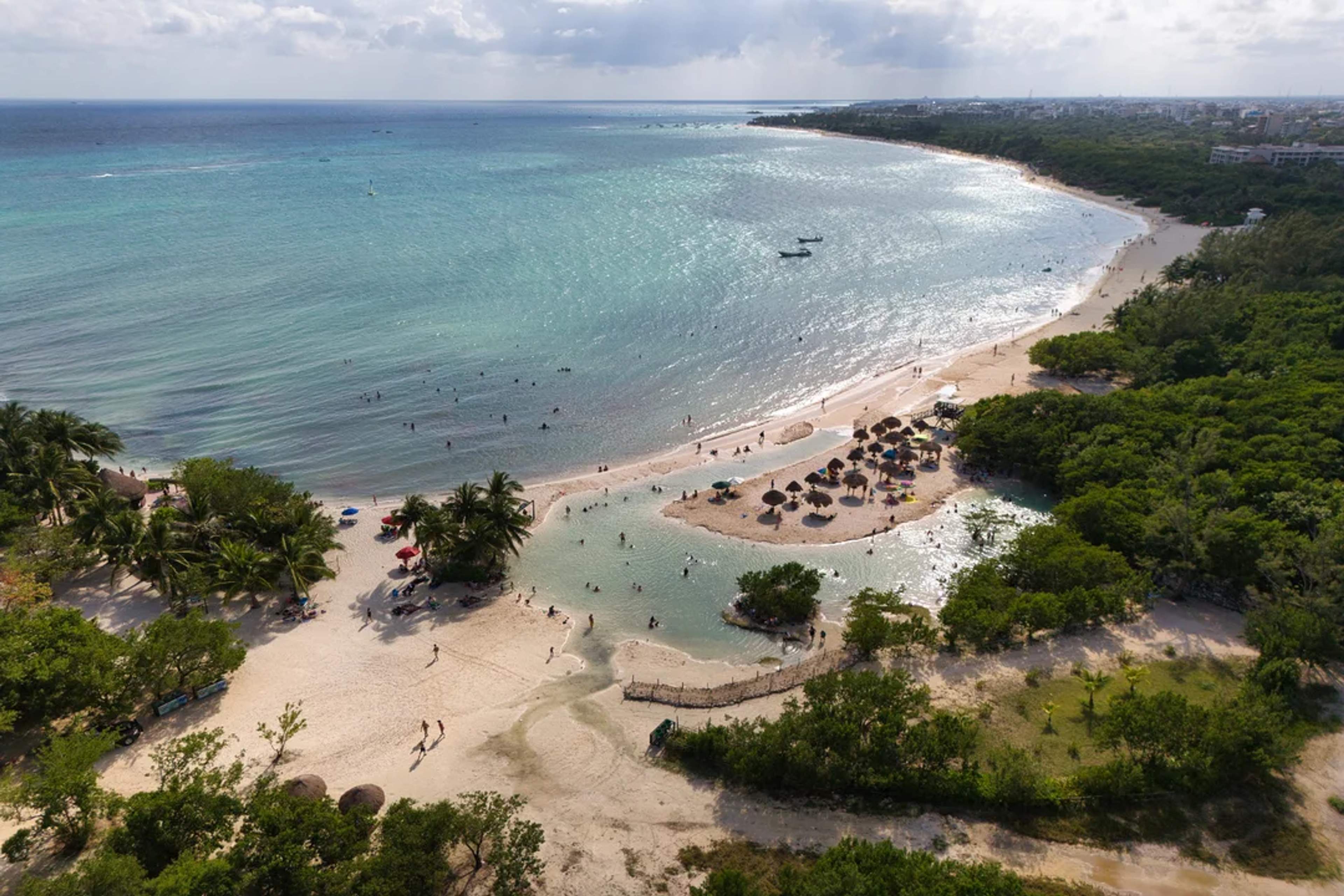 Aerial view of a tropical beach with palapas, calm waters, and lush greenery in the Riviera Maya.