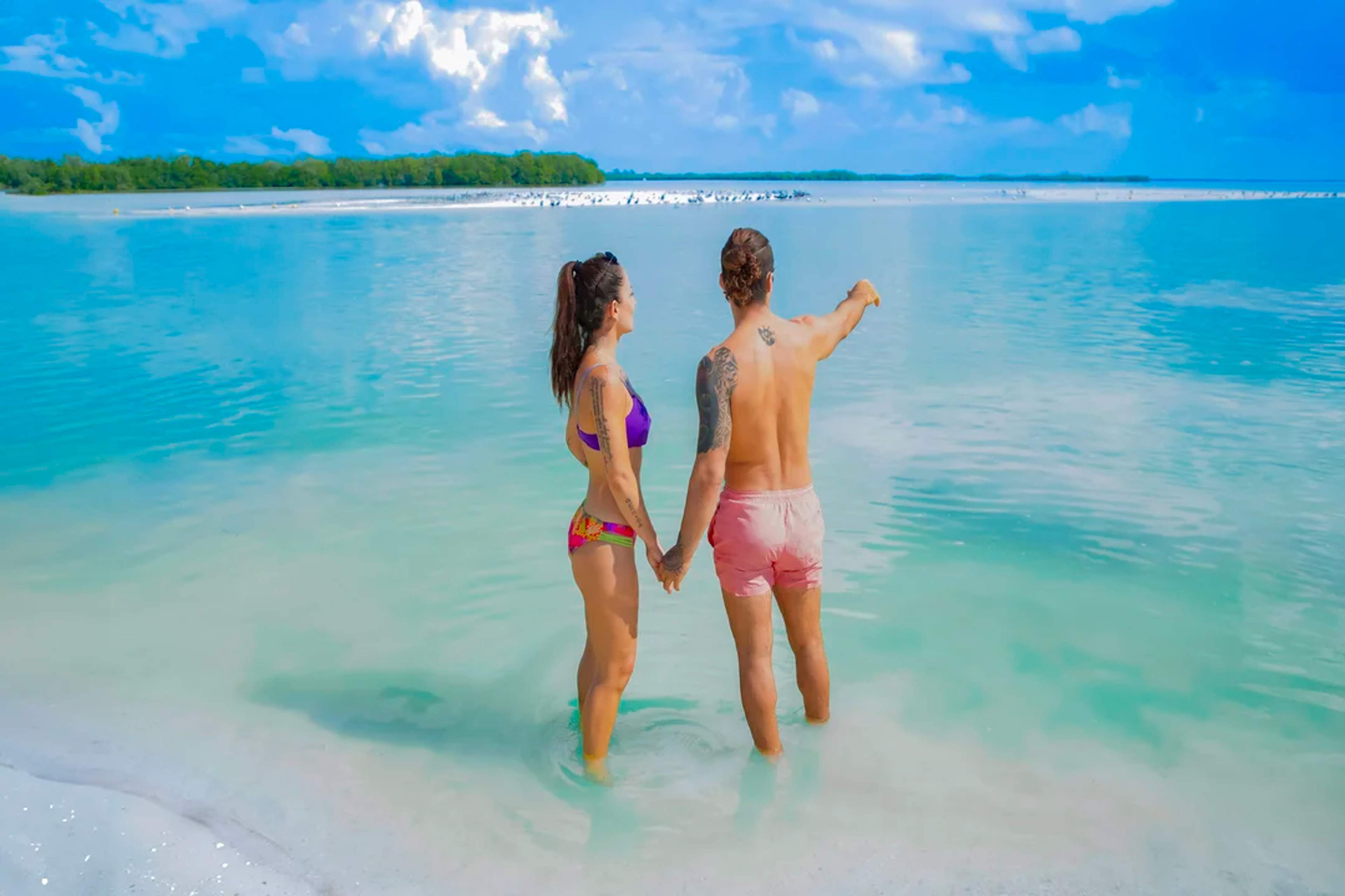 Couple holds hands in shallow turquoise waters, enjoying a peaceful view of Holbox Island.
