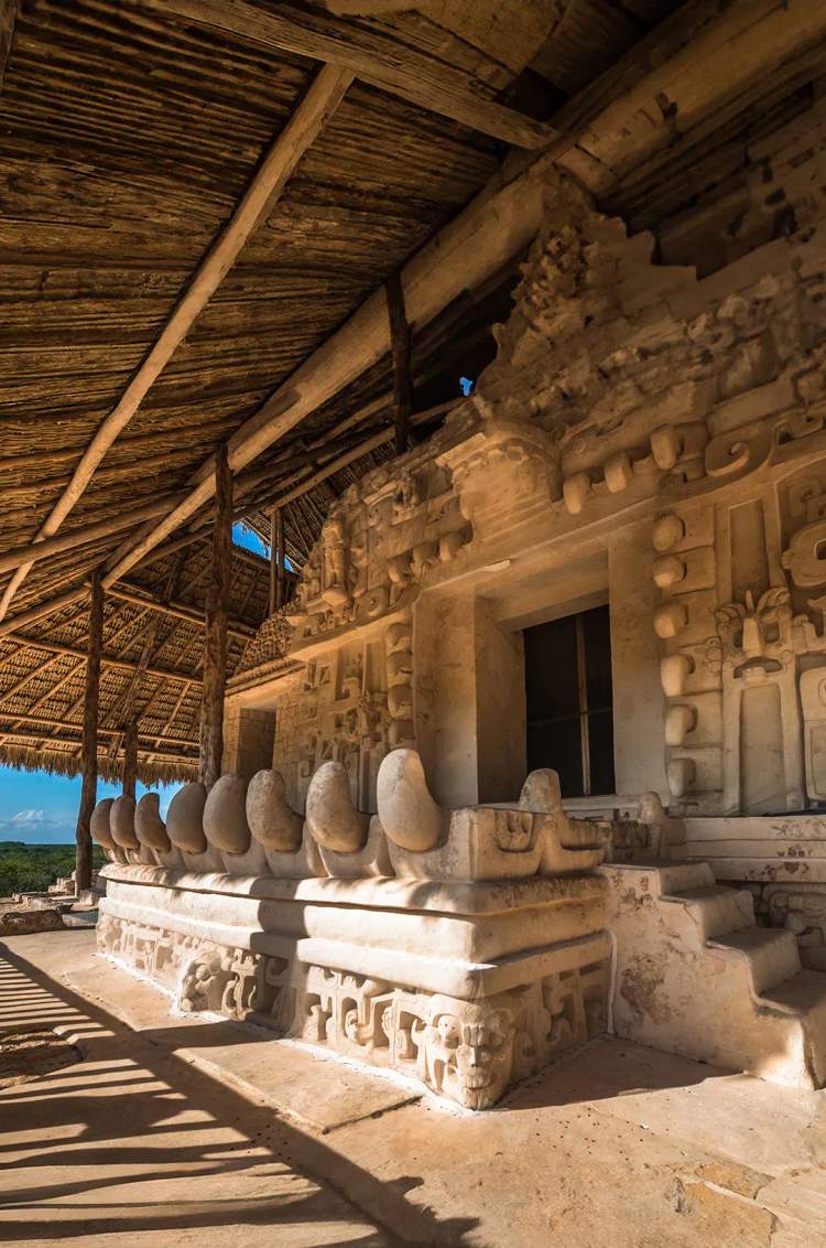Detailed stone carvings at the Acropolis of Ek Balam, under a thatched roof. 