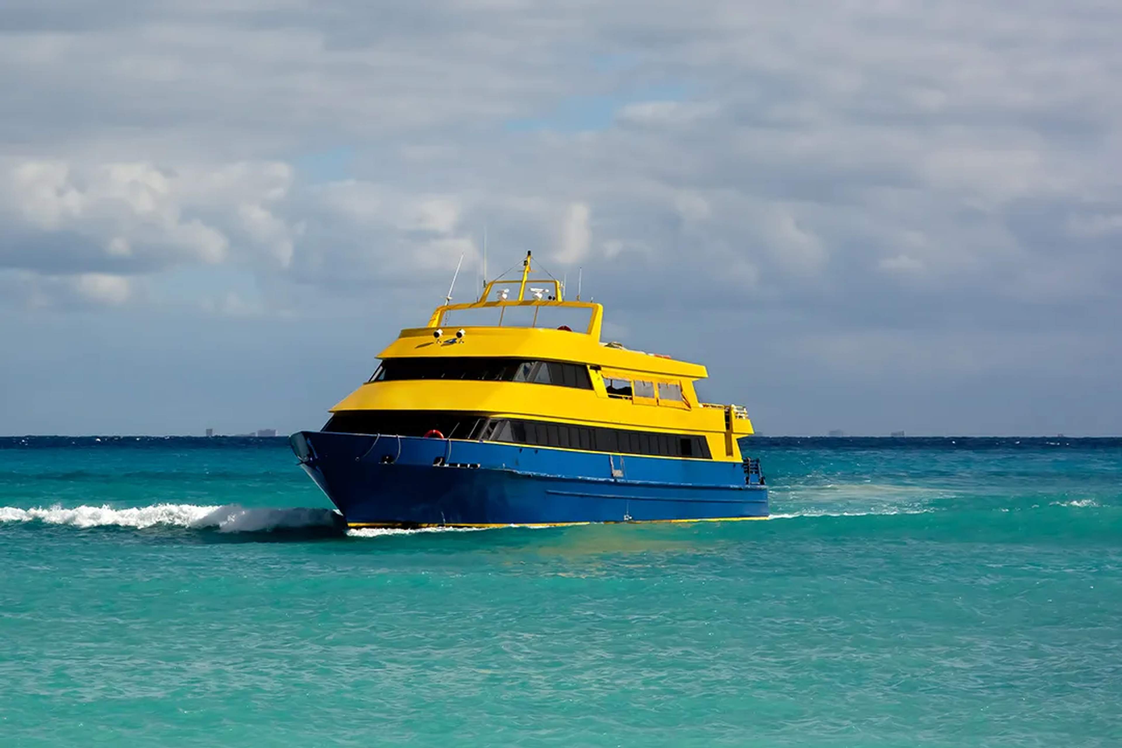 Ferry amarillo y azul navegando en aguas turquesa del Caribe bajo un cielo nublado hacia Isla Mujeres.