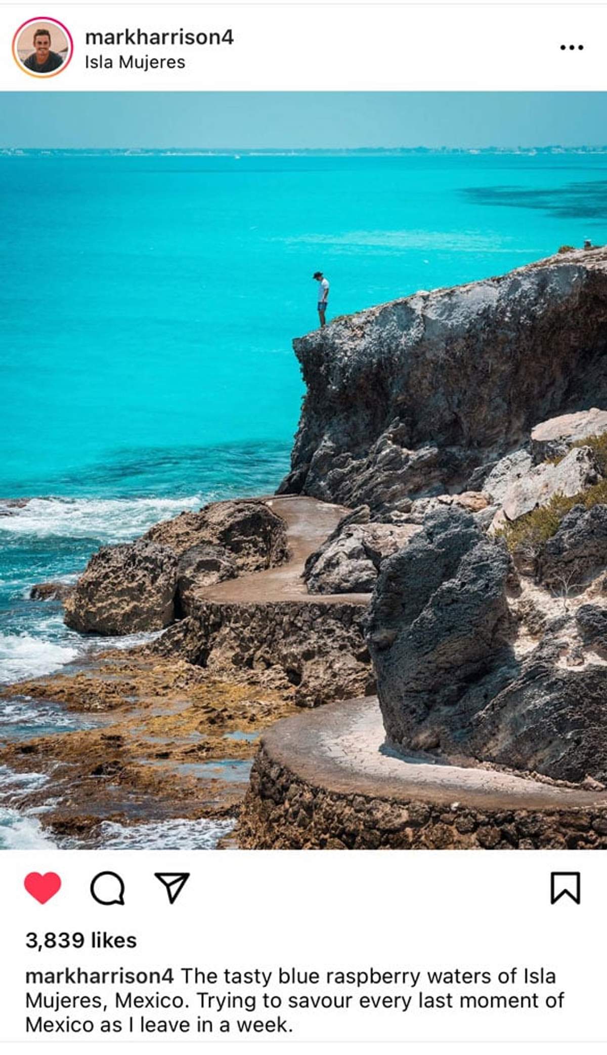 Un hombre está de pie en un acantilado rocoso con vista a las vibrantes aguas azules de Isla Mujeres, México, con la costa visible en la distancia.