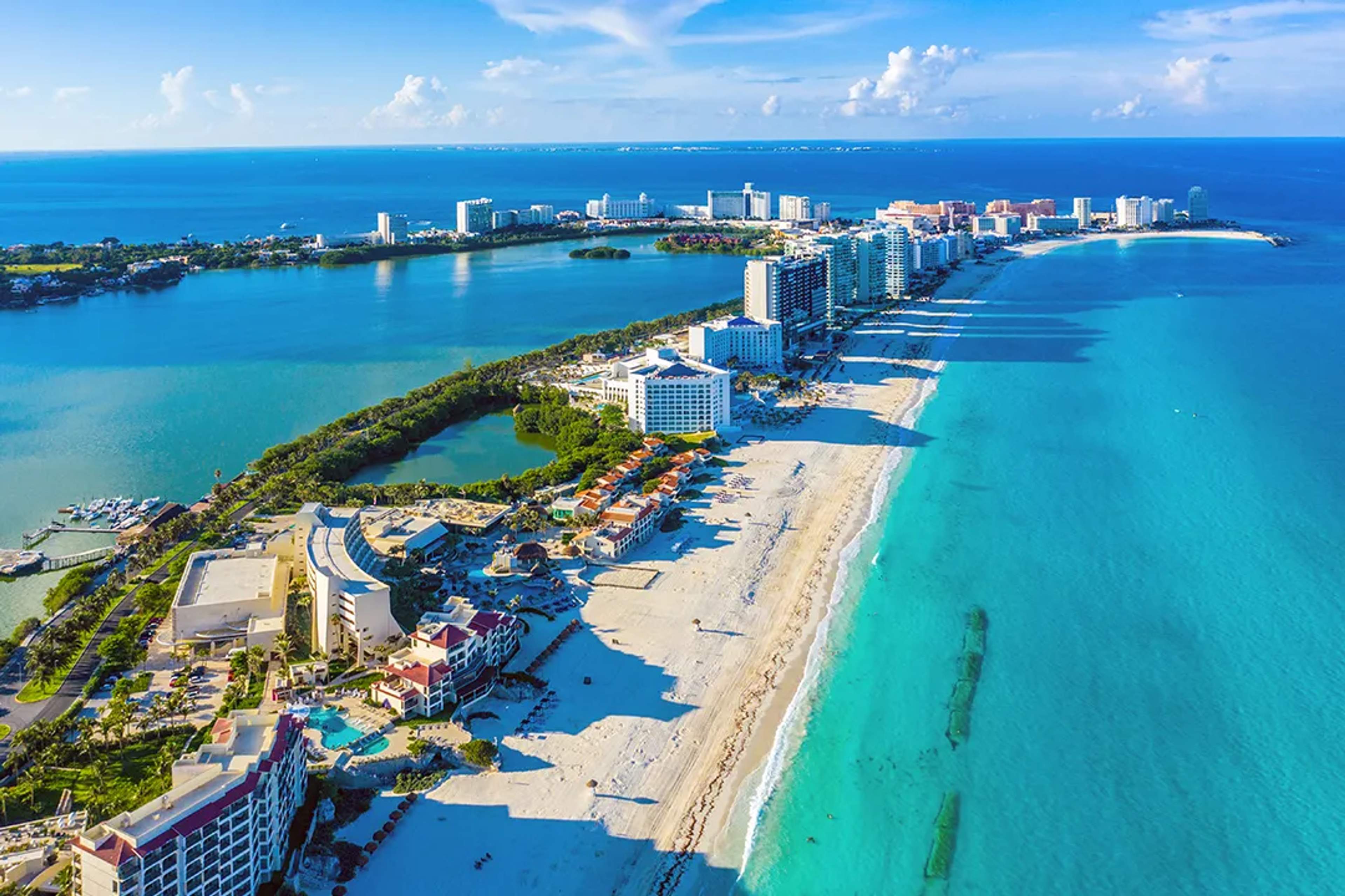 Vista aérea de la Zona Hotelera de Cancún con laguna turquesa, playas y barcos al atardecer