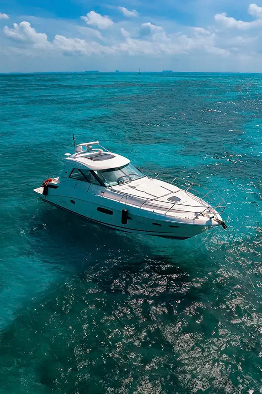 Un yate blanco anclado en aguas turquesas claras en un día soleado, con barcos distantes en el horizonte.