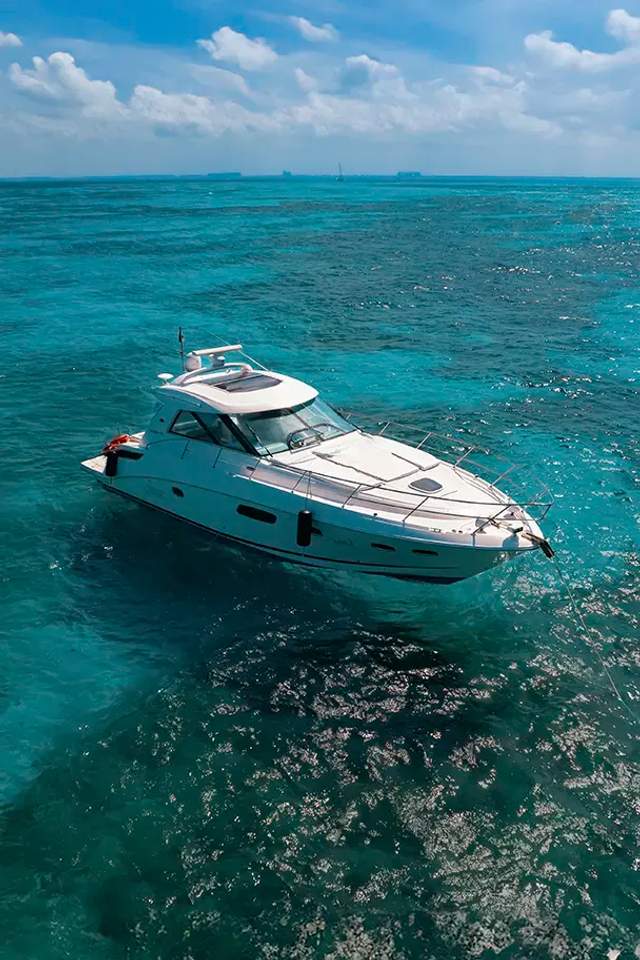 Un yate blanco anclado en aguas turquesas claras en un día soleado, con barcos distantes en el horizonte.