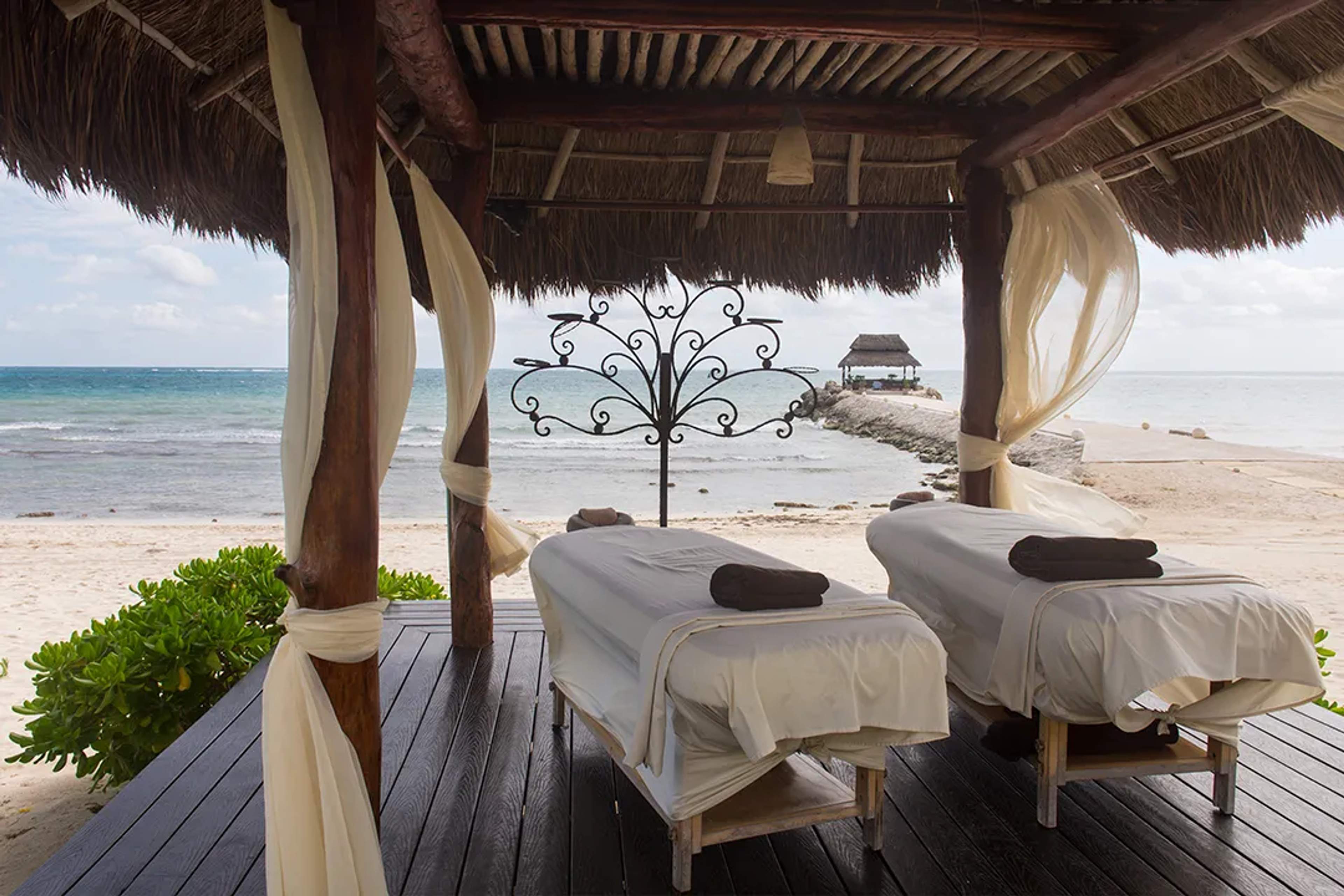 Cabaña de spa frente al mar con dos camillas de masaje y vista al océano para una experiencia relajante