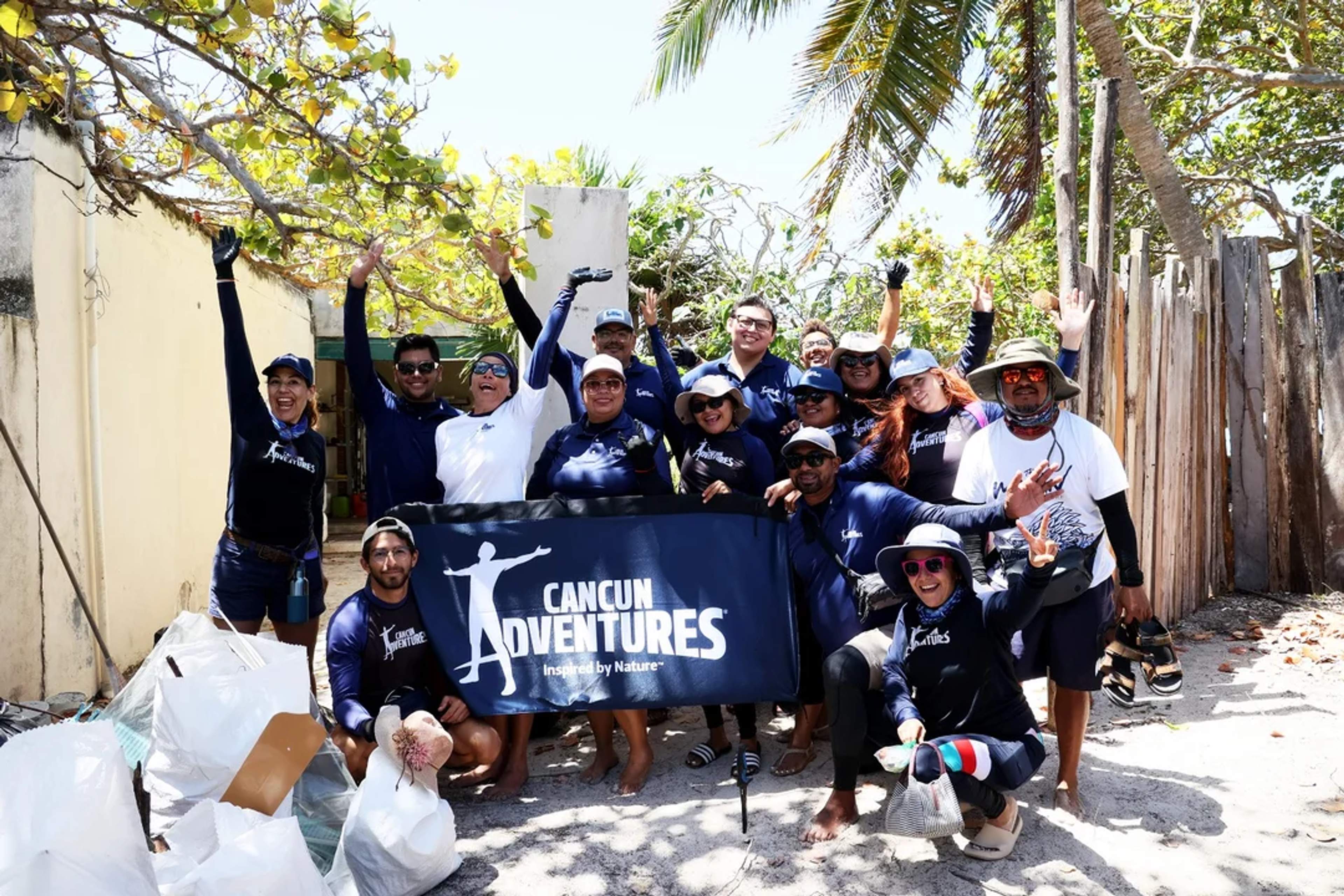 Cancun Adventures team celebrates after a beach cleanup, smiling with collected trash and a banner.