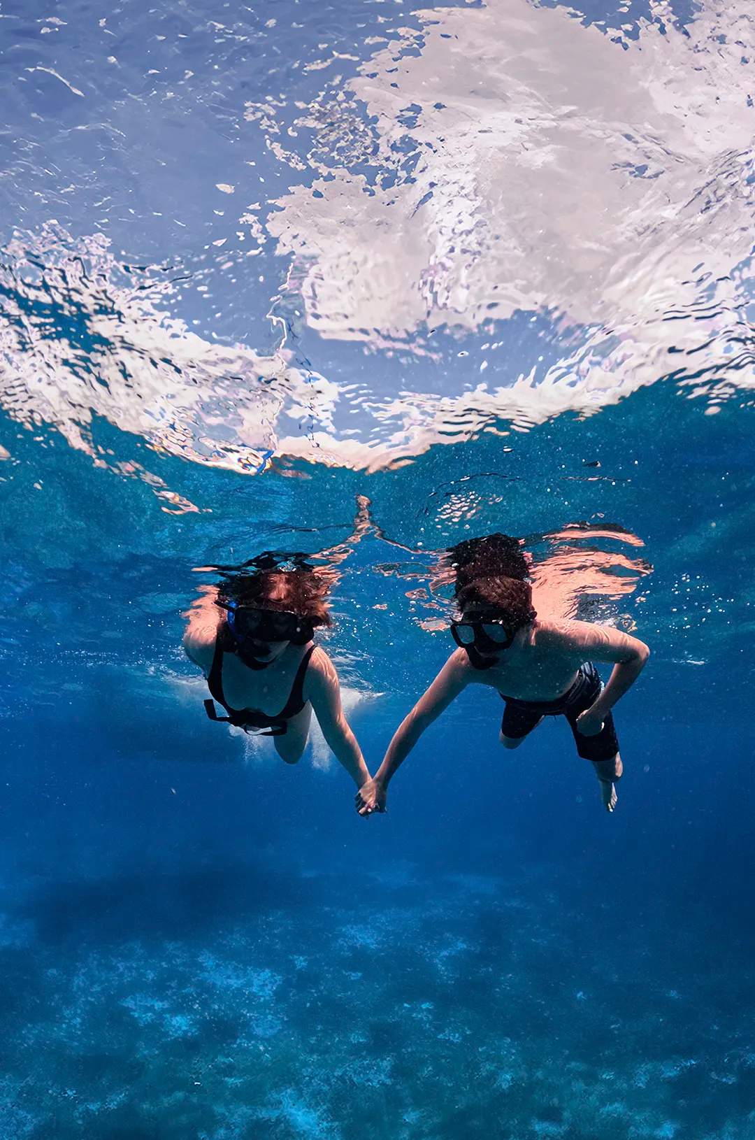 Couple snorkeling hand in hand in clear waters, exploring the underwater marine life together.