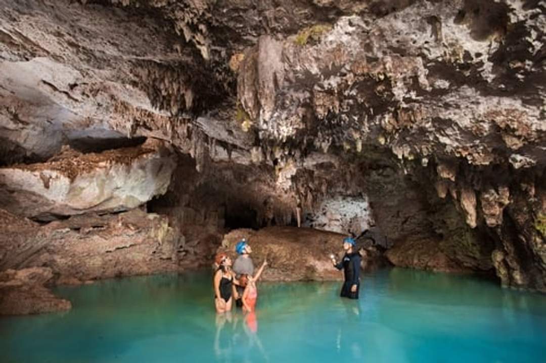 Exploring a cenote, a guide explains the cave formations and environment to a small group.