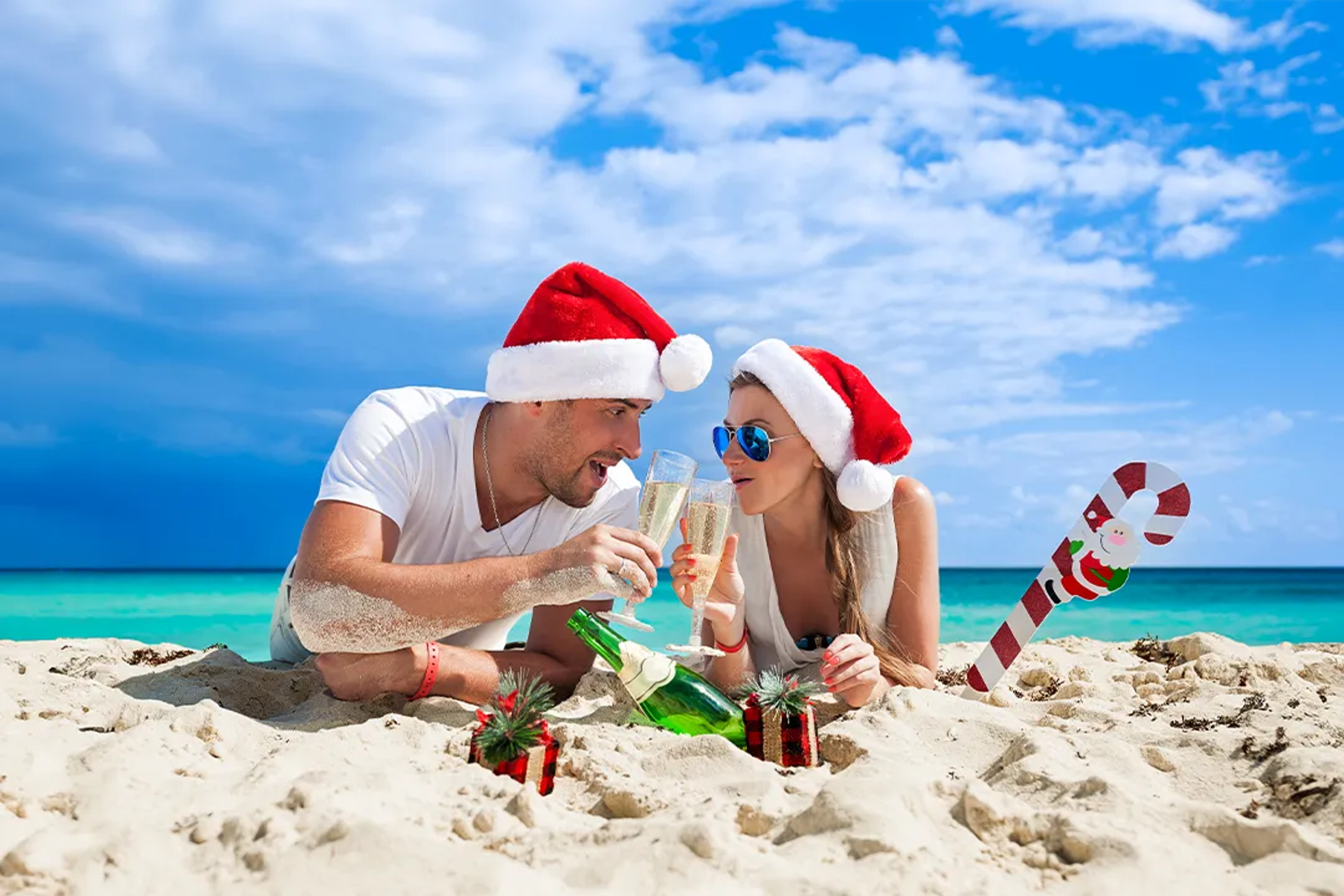 Pareja celebrando Navidad en la playa de Cancún, con gorros de Santa y brindando con champaña.