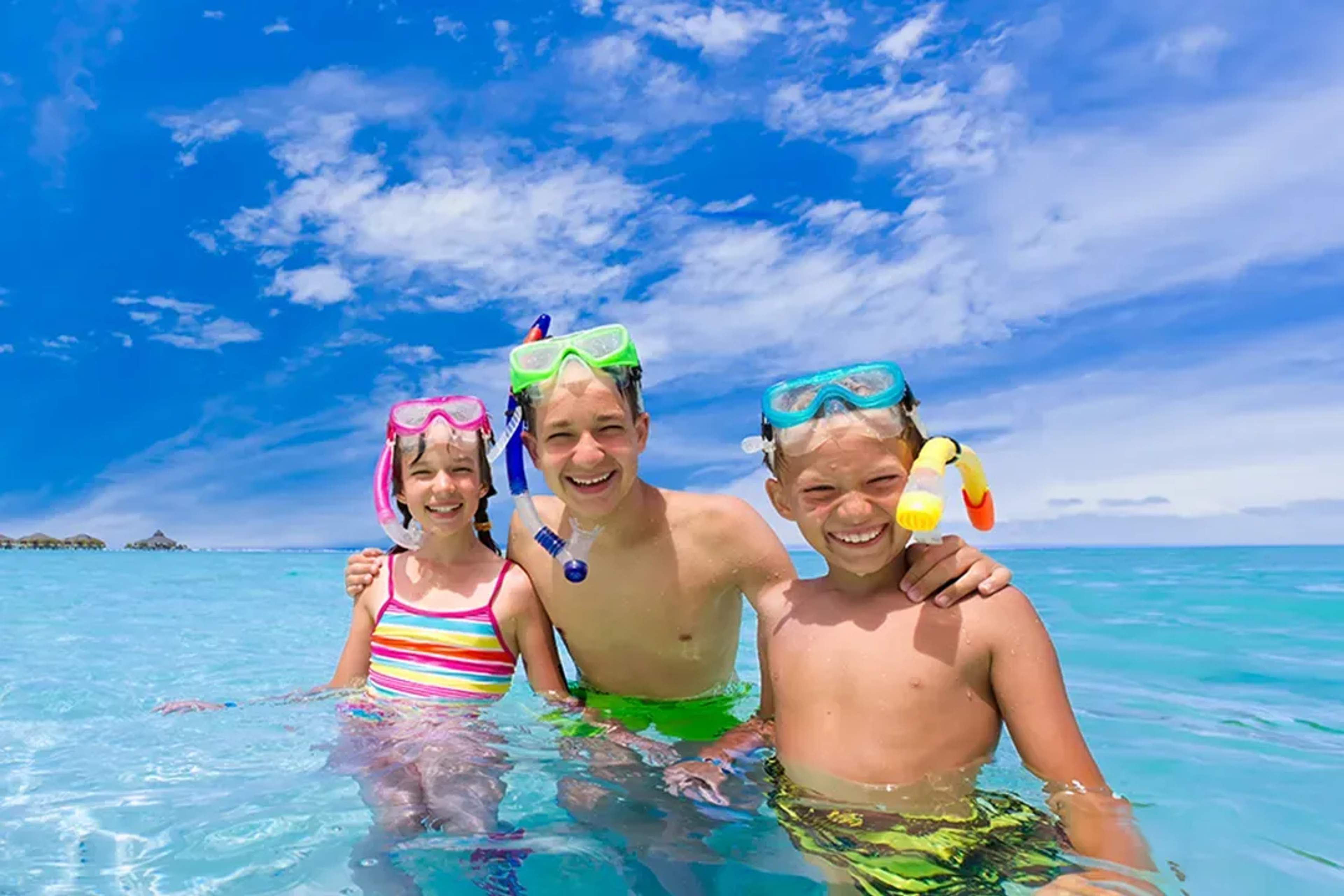 Tres niños felices practicando snorkel en aguas turquesa bajo un cielo azul brillante en Cancún.