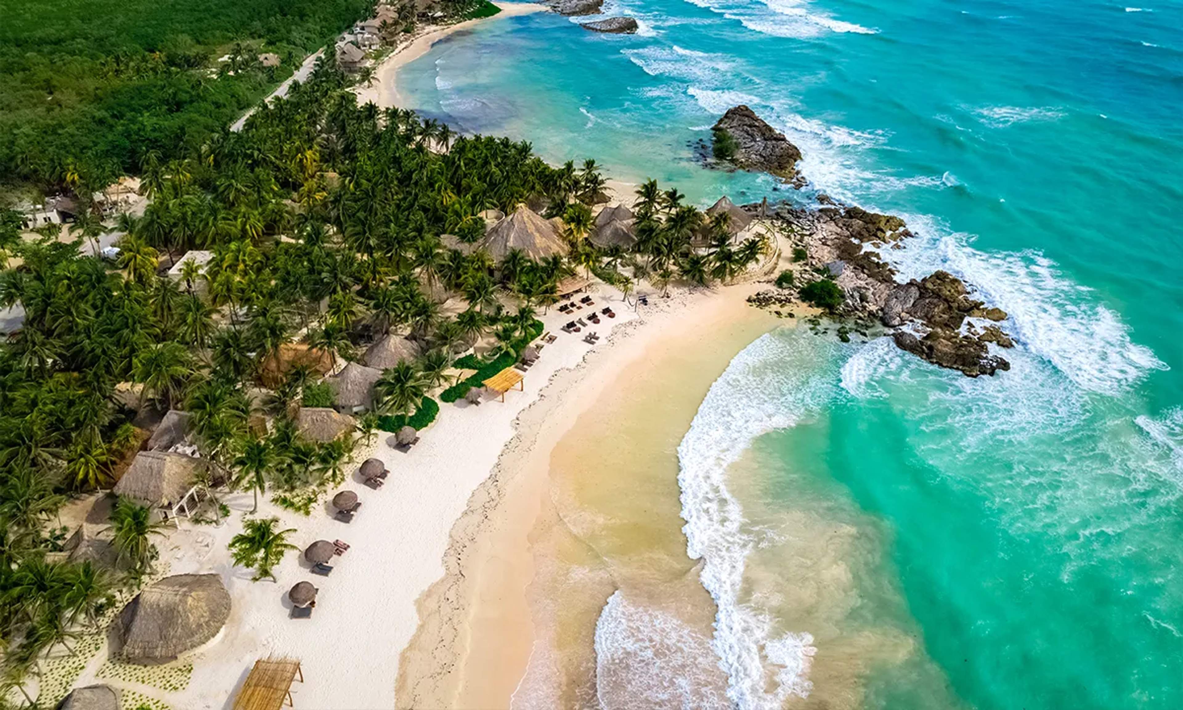 Paradise Beach in Tulum features soft white sand, turquoise waters, and lush palm trees, offering a serene Caribbean escape.
