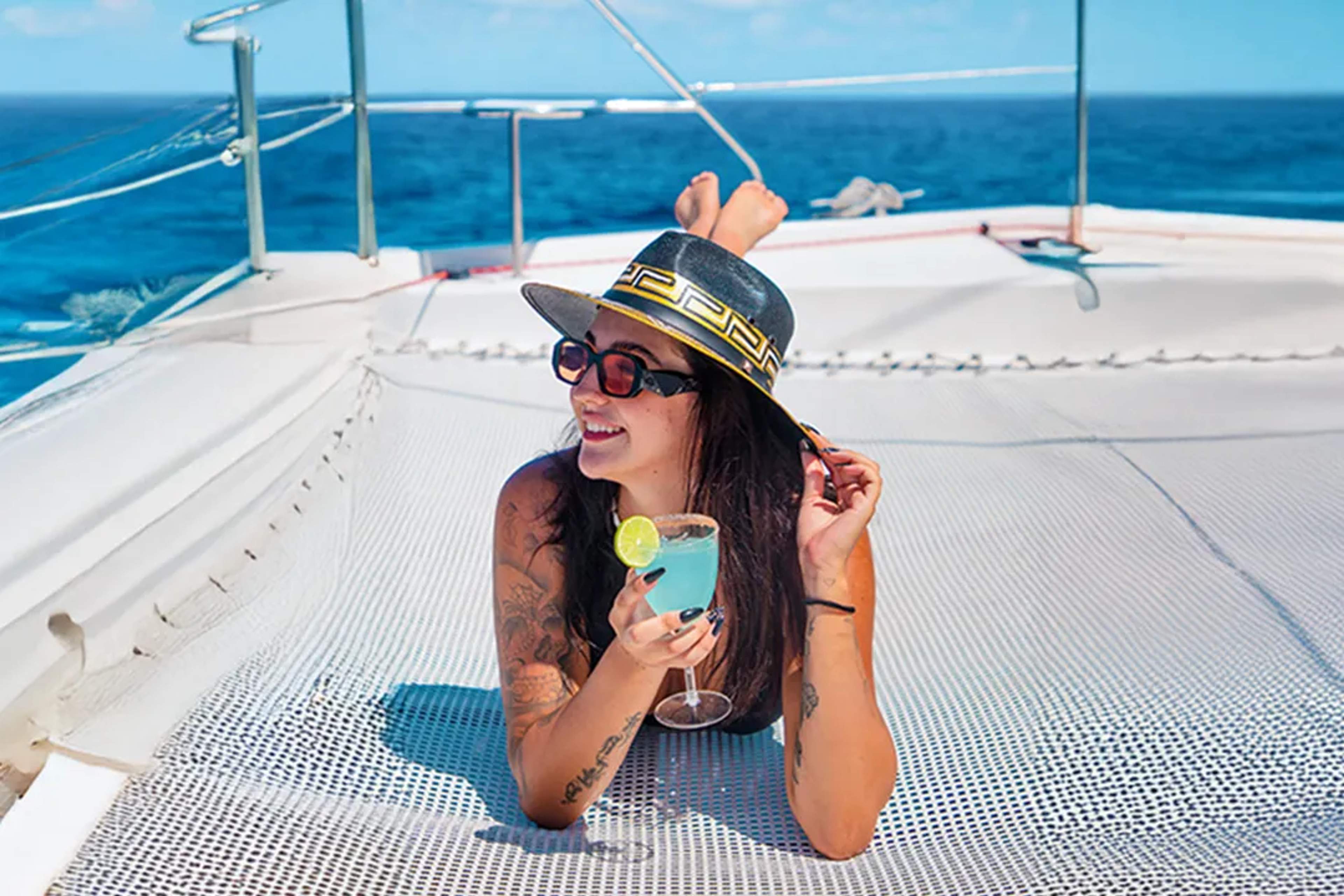 Woman relaxing on a catamaran net in the Caribbean Sea, enjoying a sunny sailing experience with Cancun Adventures.