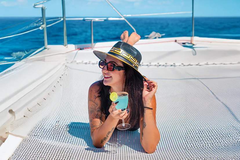 Woman relaxing on a catamaran net in the Caribbean Sea, enjoying a sunny sailing experience with Cancun Adventures.