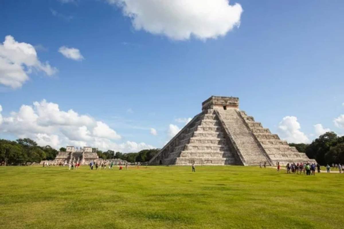 Tourists walking near the iconic El Castillo pyramid at Chichen Itza on a sunny day with a clear sky.