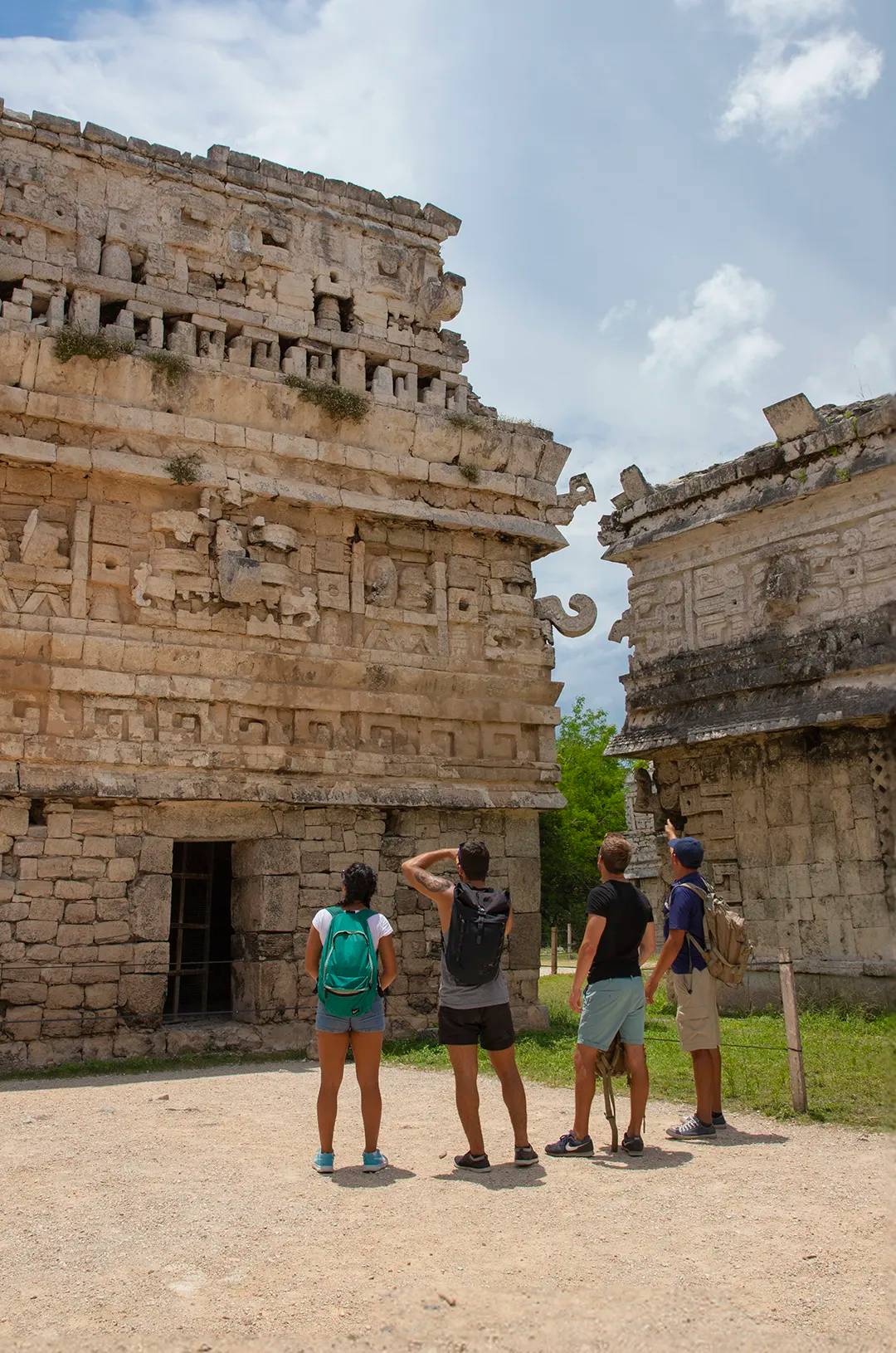 Group of tourists with backpacks exploring ancient Mayan ruins at Chichen Itza, admiring the detailed stone carvings.