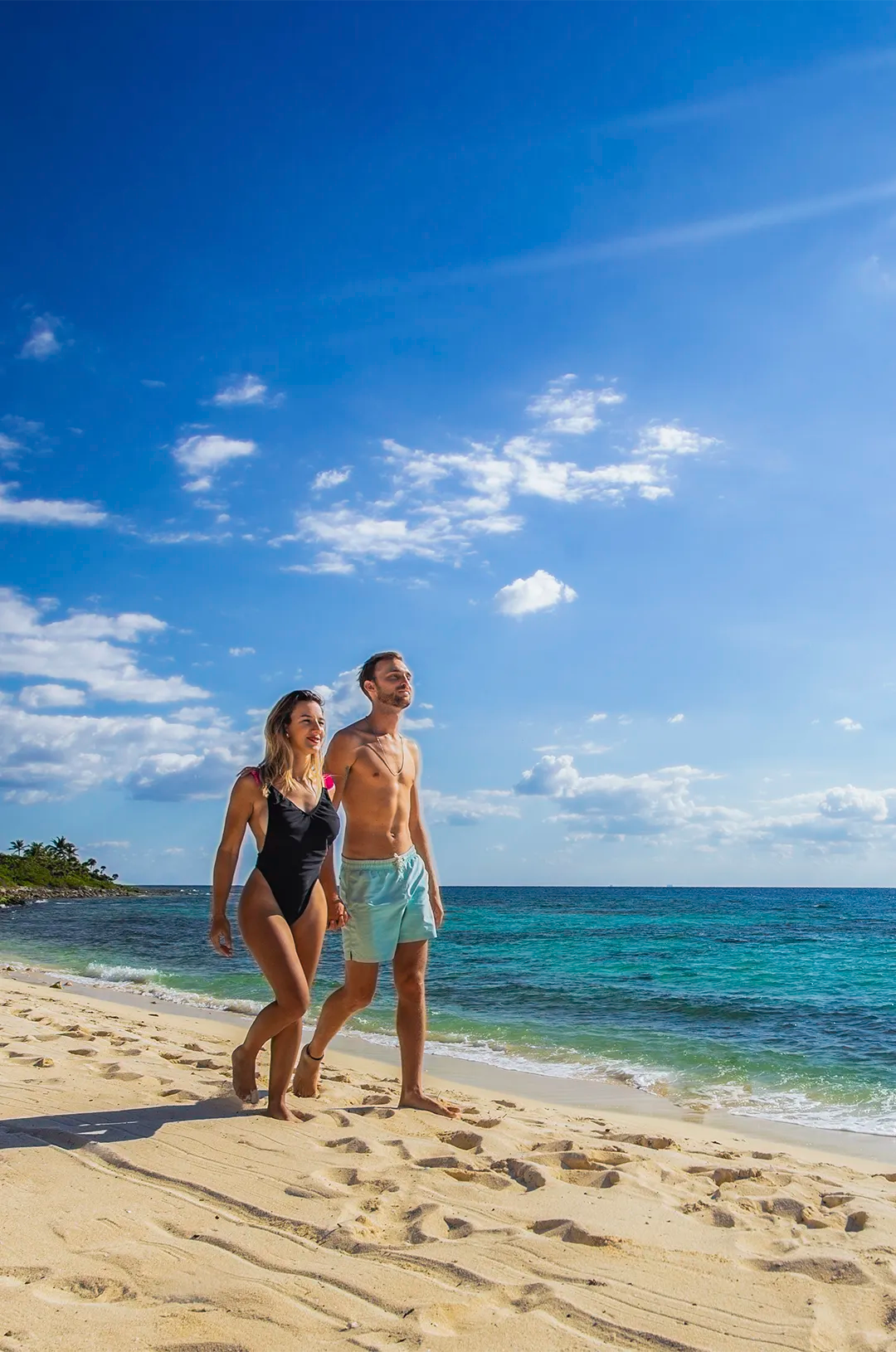 Couple walking along the sandy beach during a beach club tour in Tulum, under a clear sky.