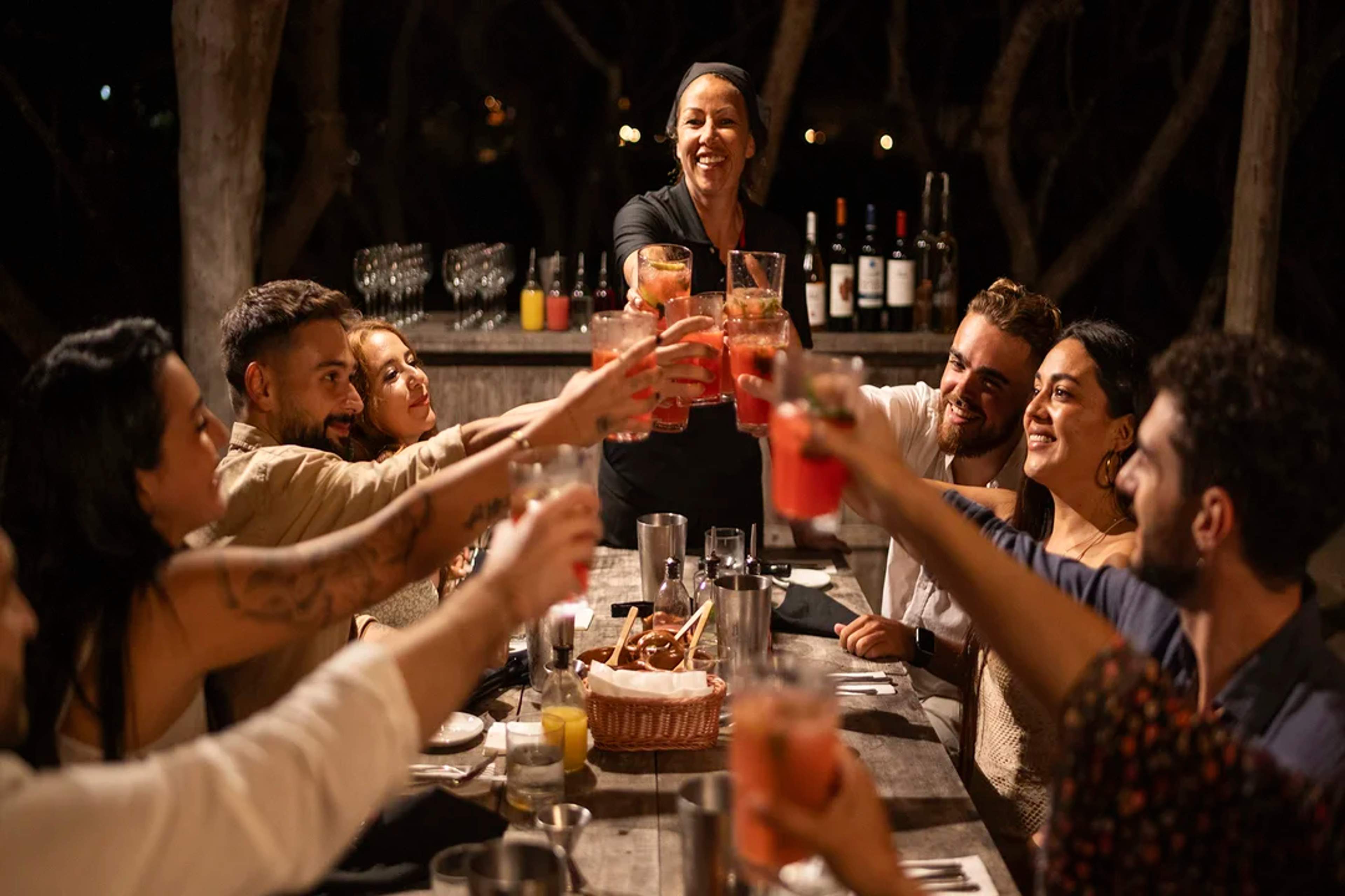 Grupo de amigos brinda con bebidas coloridas en una cena al aire libre, compartiendo risas y buenos momentos.