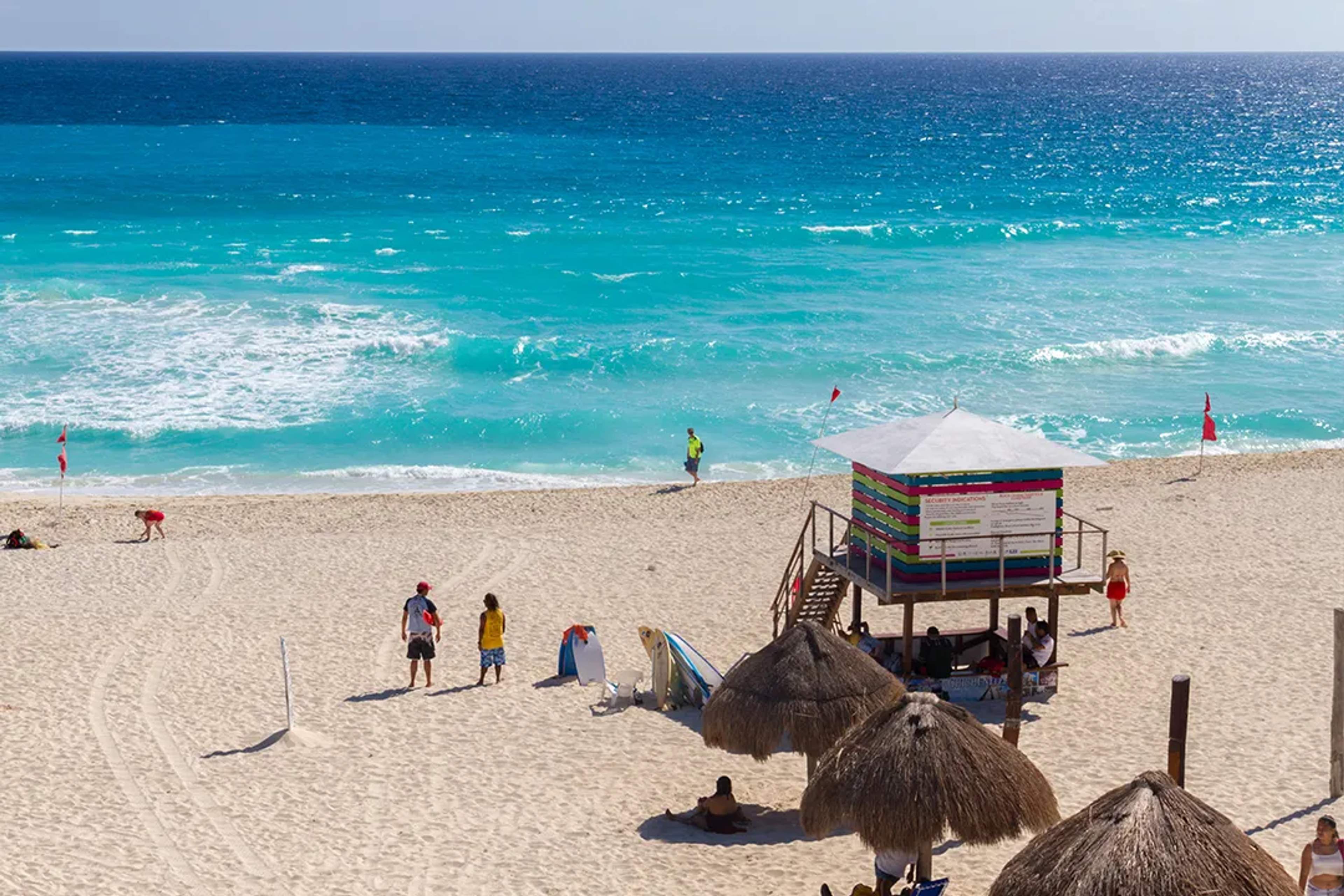 Cancun beach with turquoise waves, lifeguard tower, and visitors enjoying the sunny white-sand shore