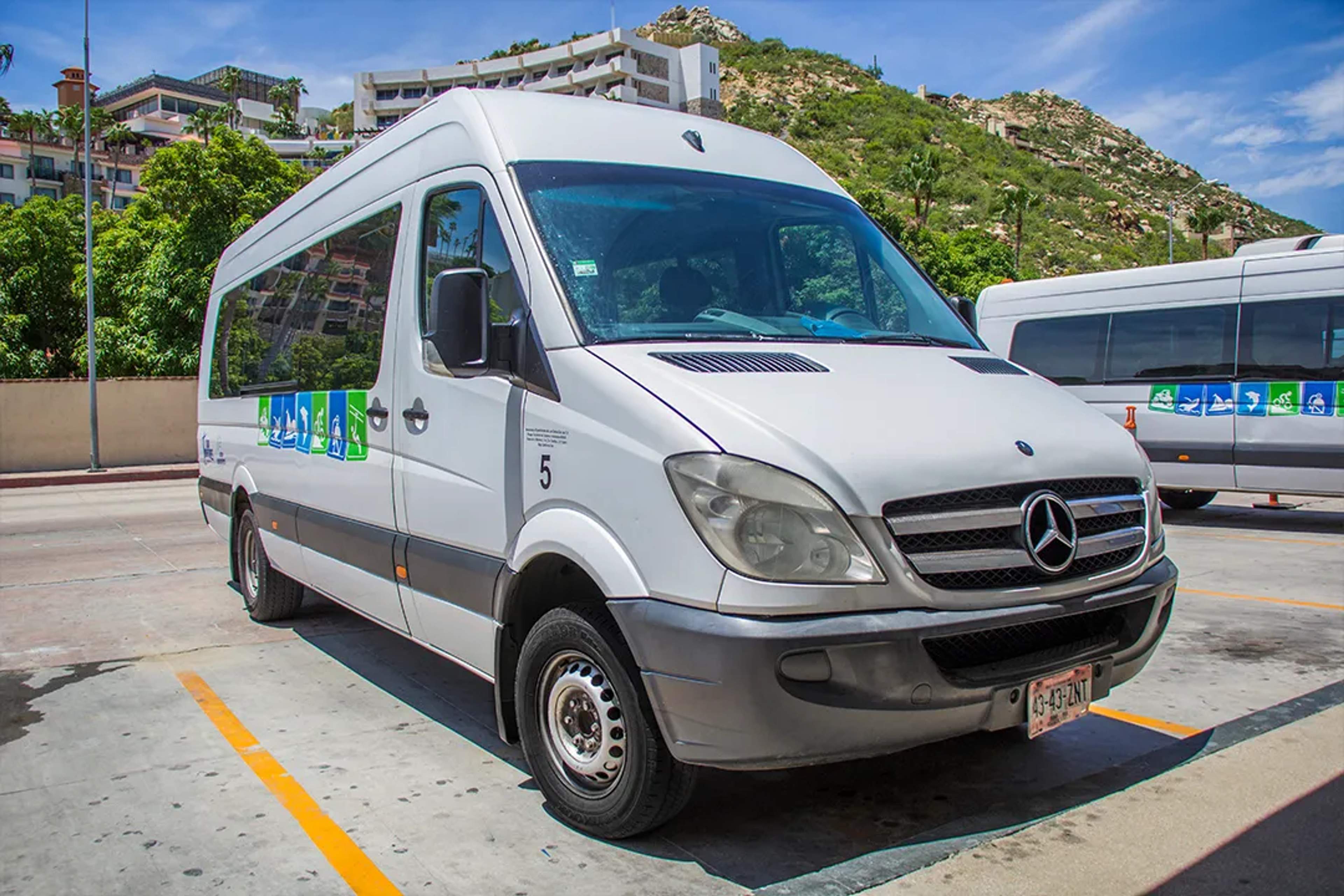 White Mercedes van for tourist transfers parked under the sun in a scenic coastal town.