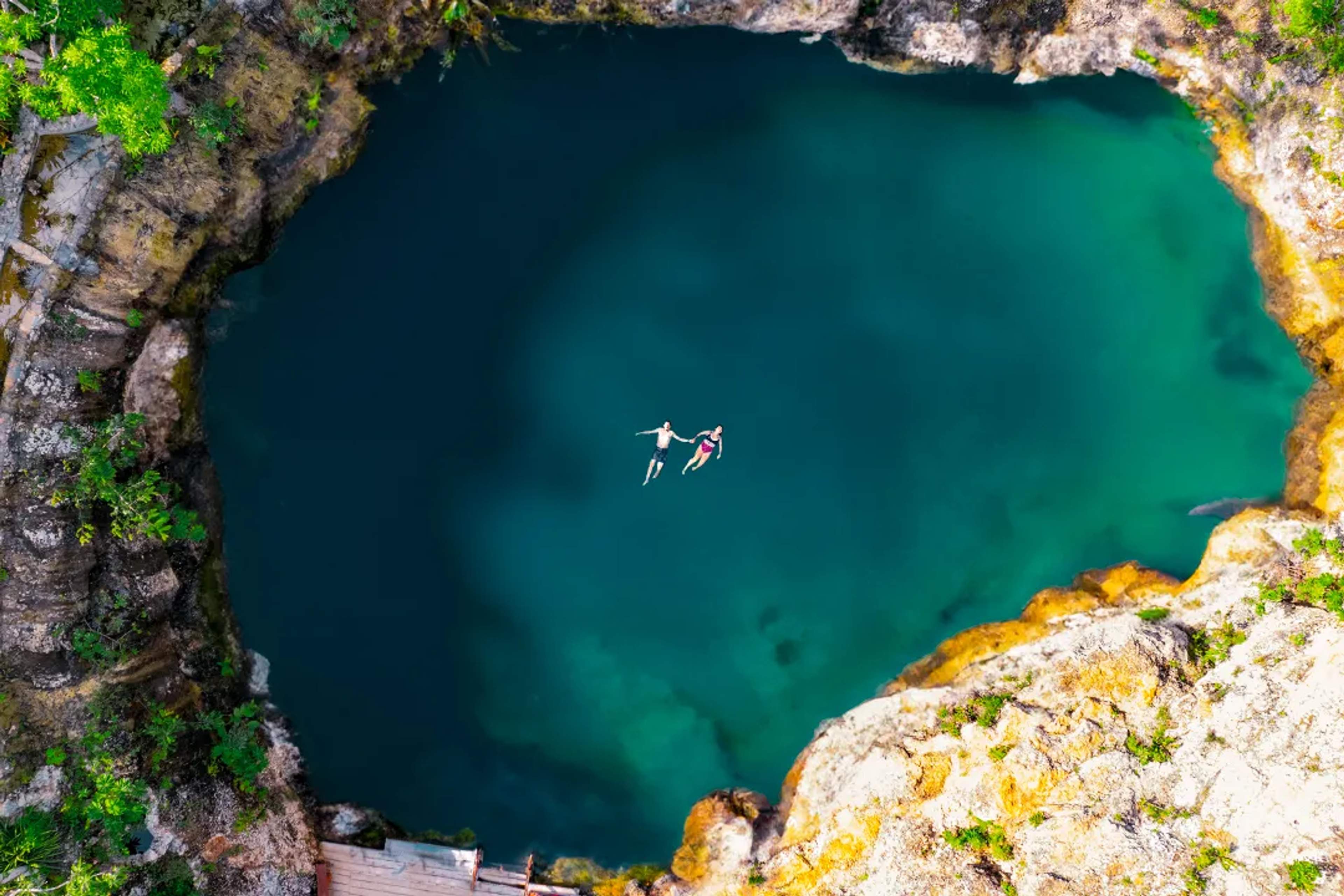 Couple swimming in a cenote with turquoise water surrounded by rocky walls and lush greenery in Riviera Maya