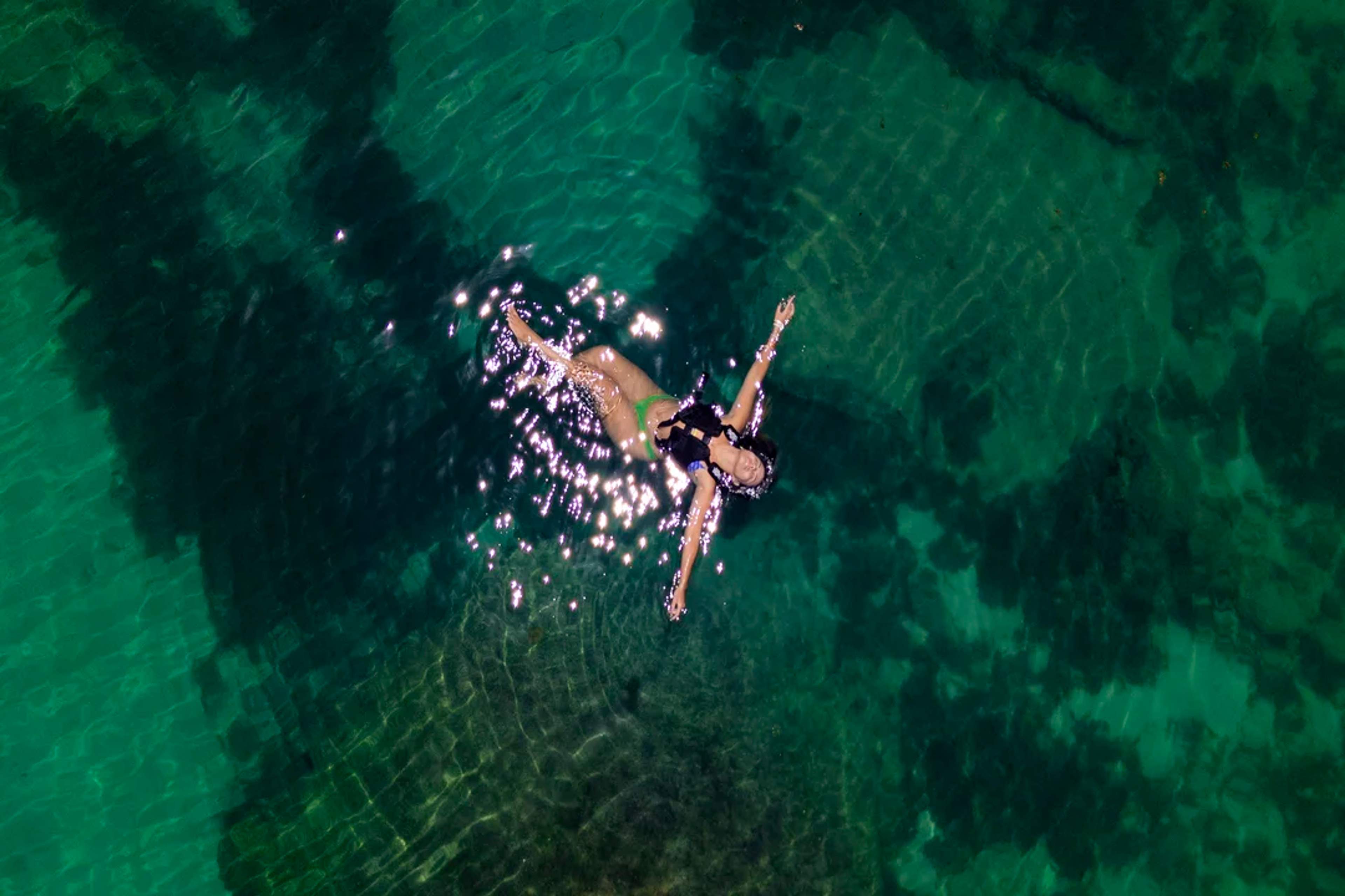 Flota libre en las aguas esmeralda de Yal-Ku, bañada por el sol y rodeada de belleza submarina.