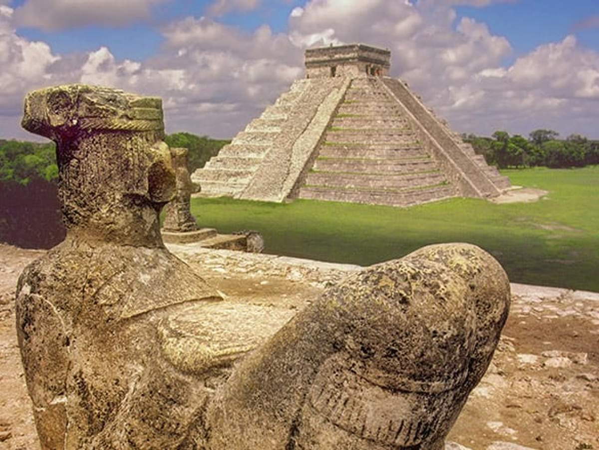Ancient statue and pyramid at Tulum ruins, showcasing Mayan architecture.