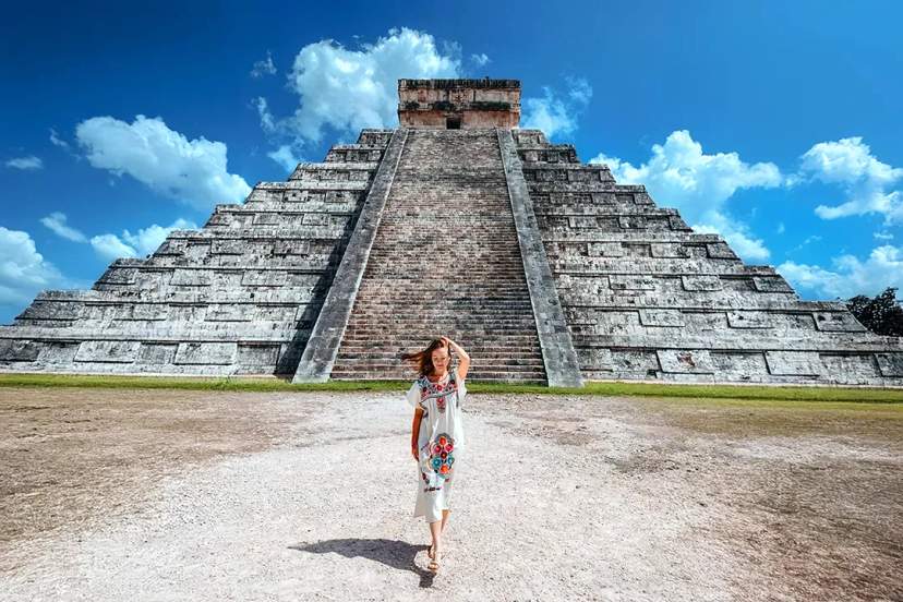 Pirámide de Chichén Itzá bajo un cielo azul, rodeada de vegetación verde.