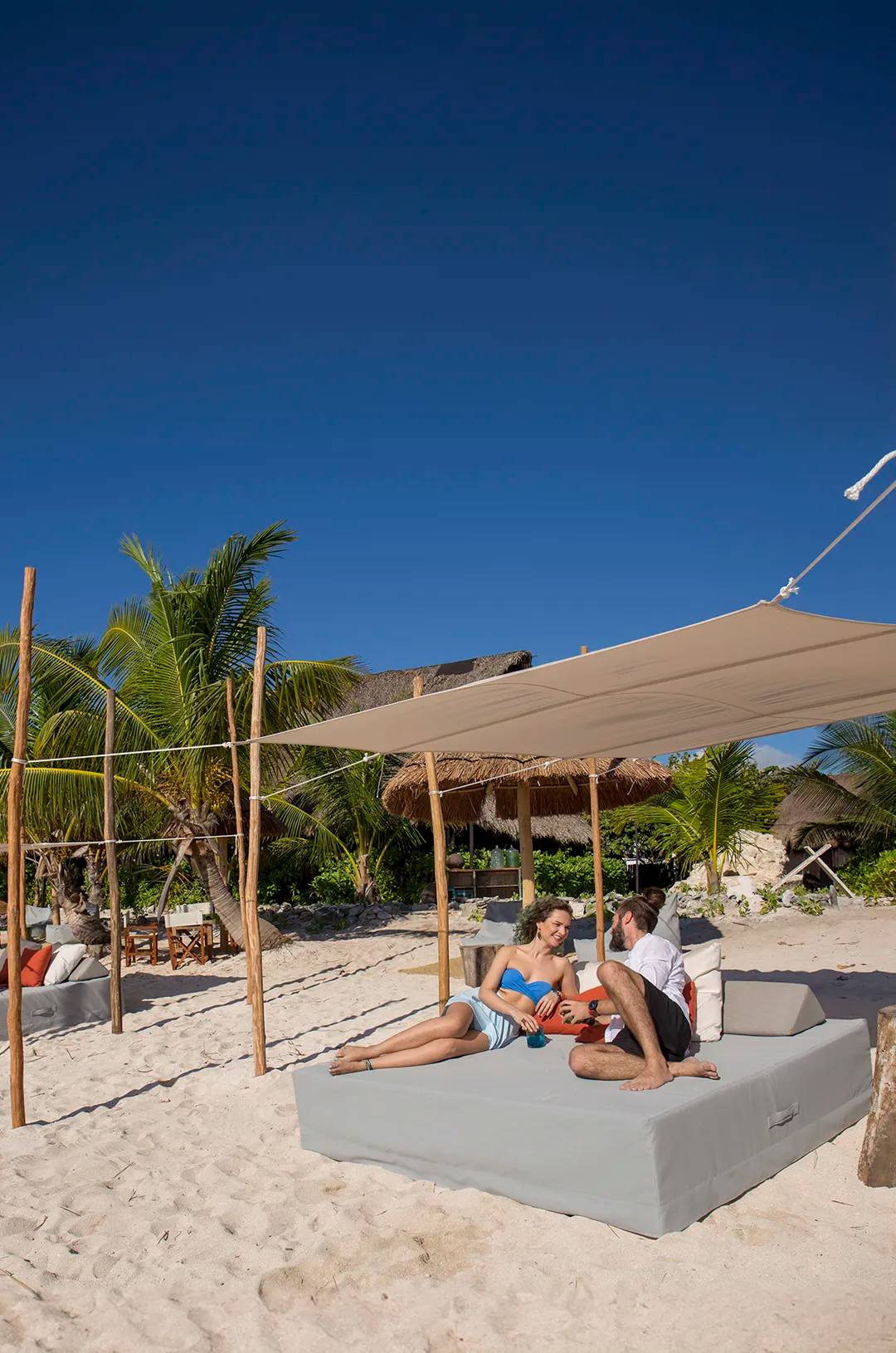 Pareja relajándose bajo la sombra de una cama balinesa en la playa en Cancún.