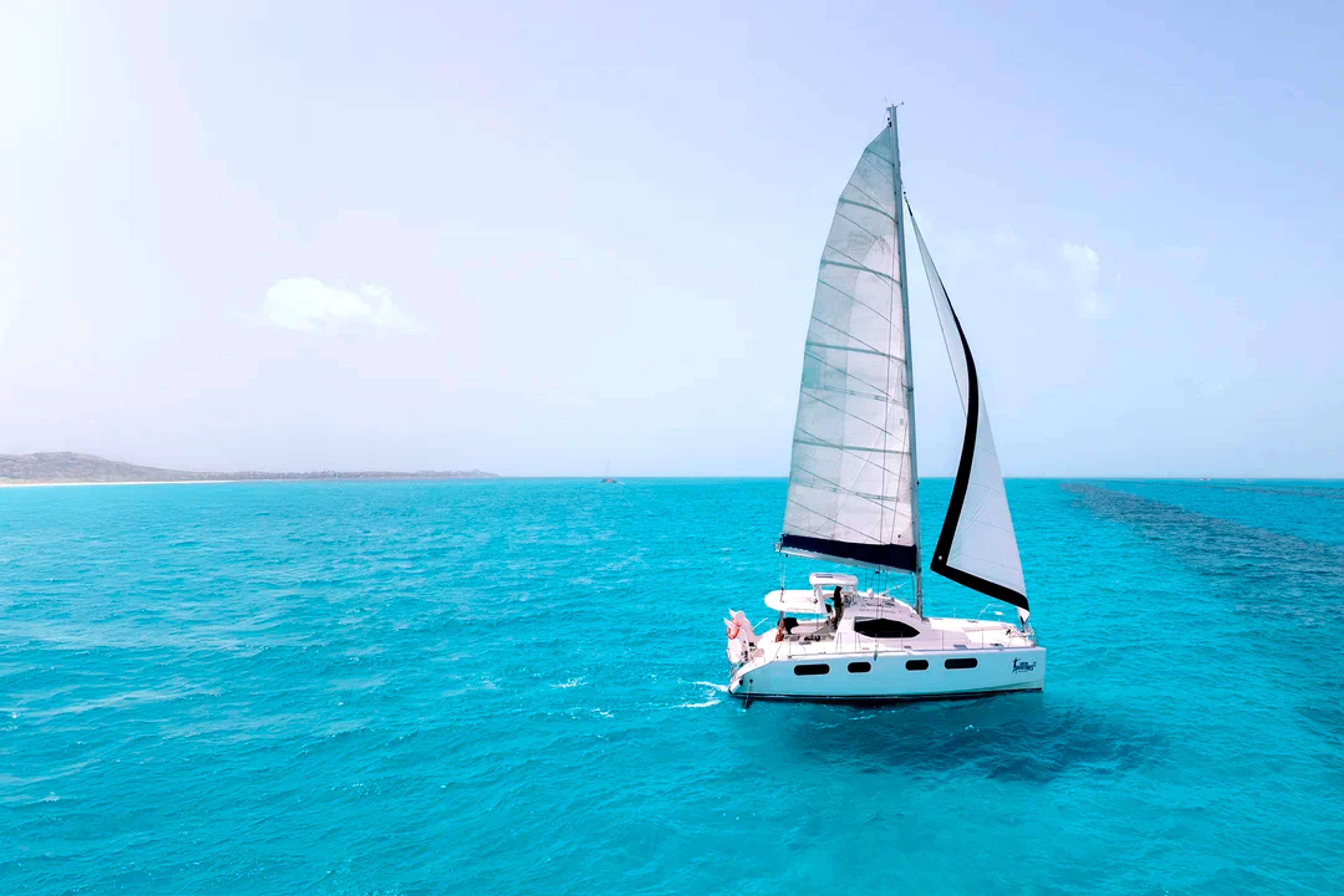 White sailboat glides over turquoise waters under a clear sky, creating a serene seascape.