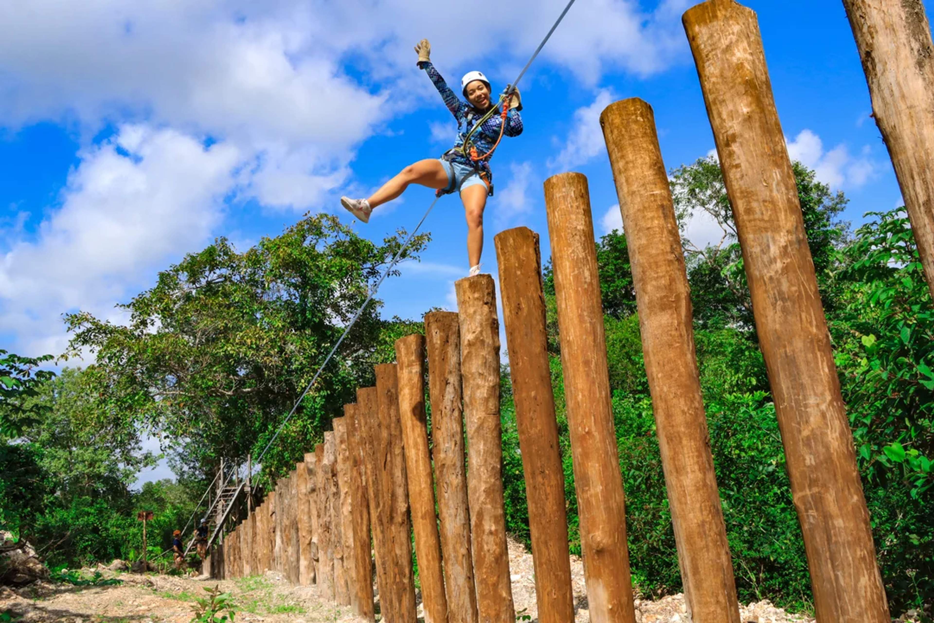 Mujer disfruta una aventura en circuito aéreo, equilibrándose sobre troncos con equipo de seguridad.