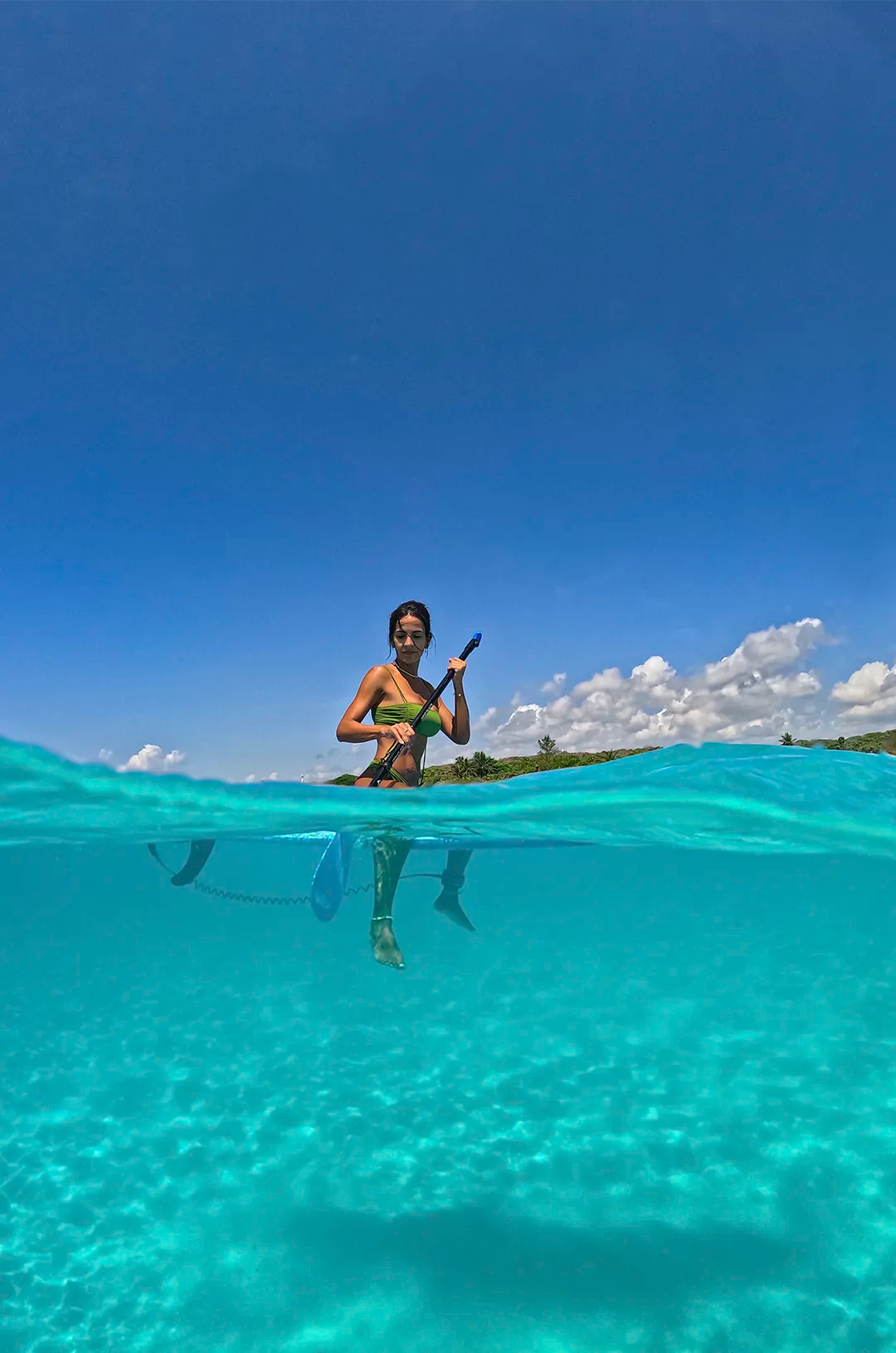 Woman paddleboarding on clear turquoise waters under a bright blue sky.