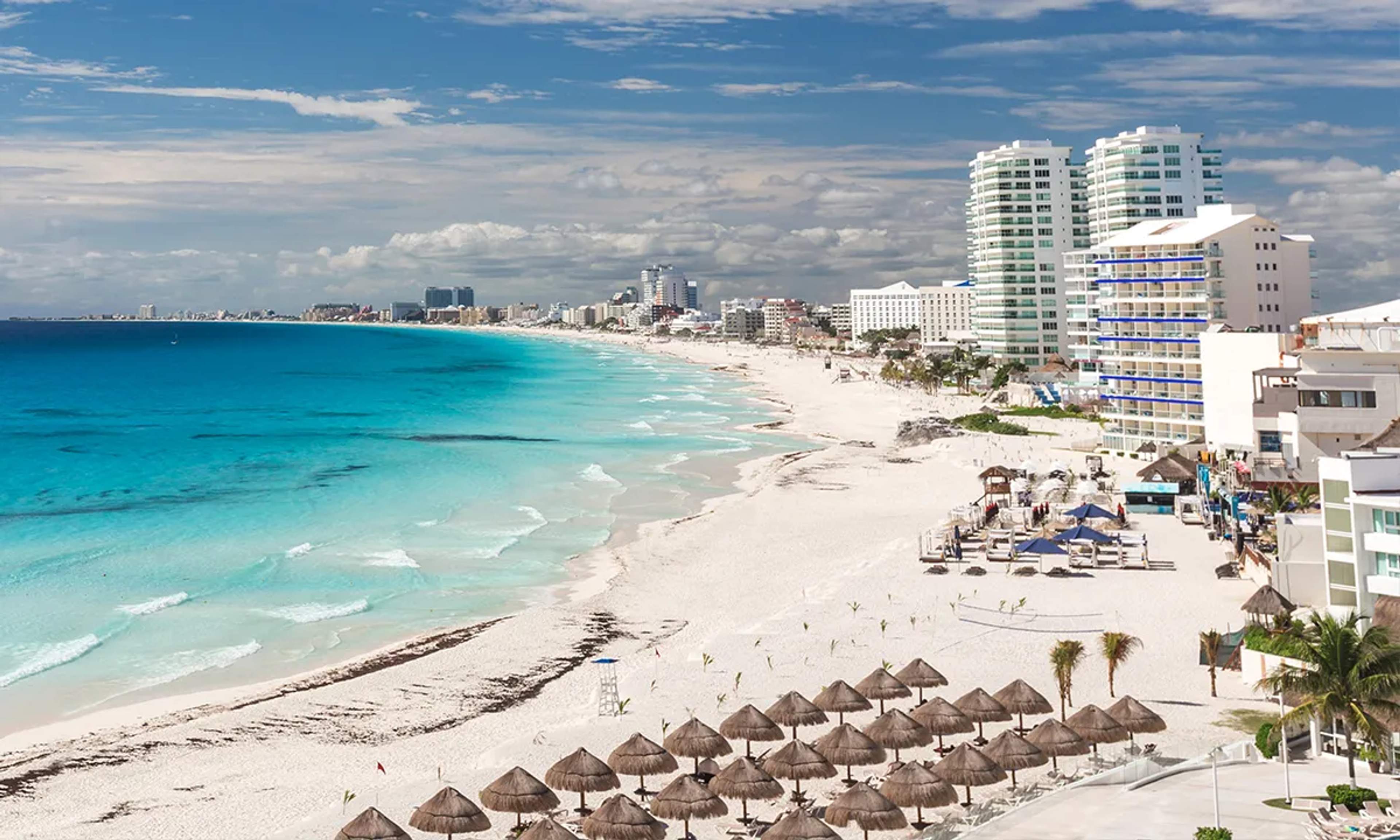 White sand beach with turquoise waters in Cancun, surrounded by hotels and umbrellas, perfect for a tropical getaway.