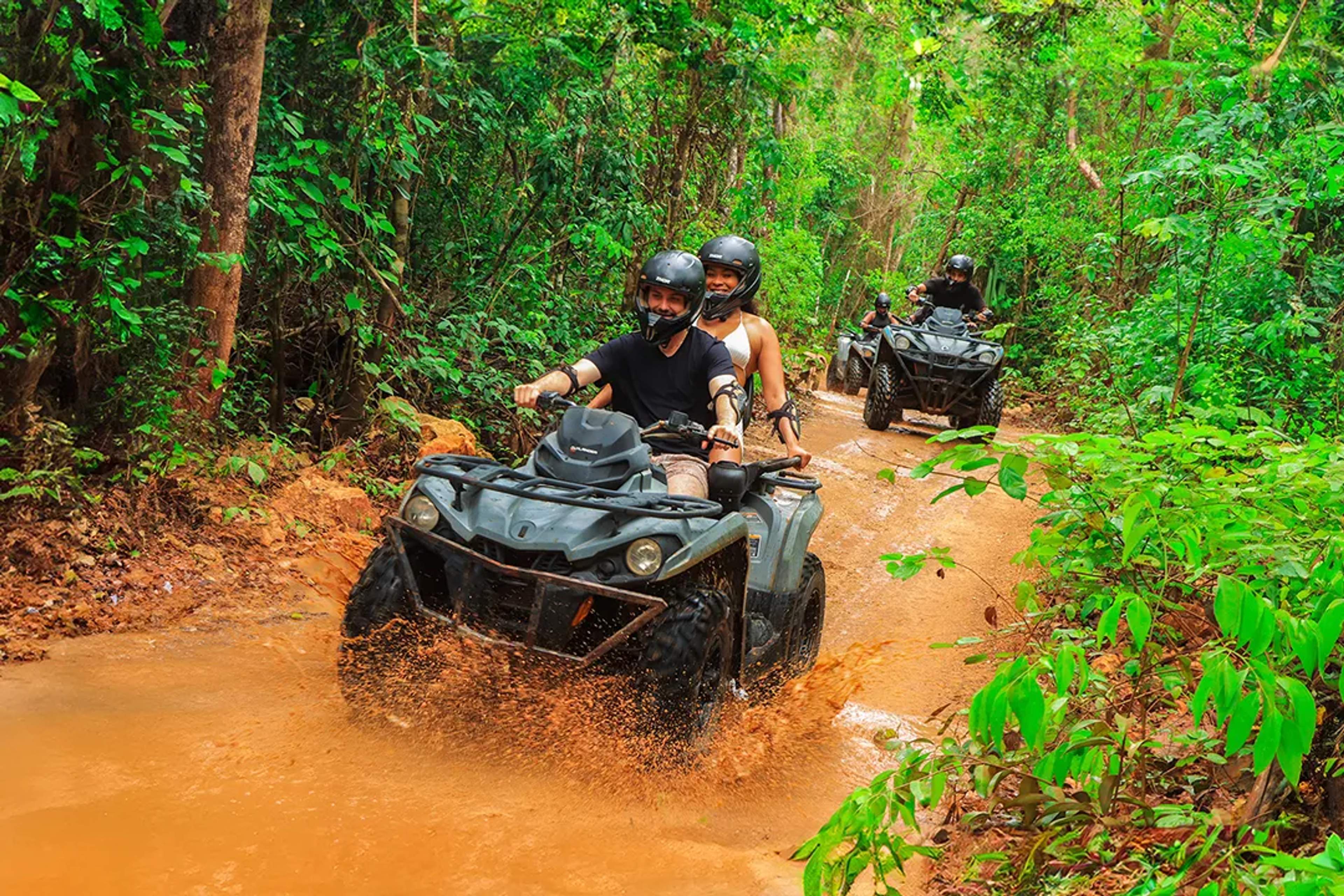 ATV riders splashing through jungle trails during the Adrenaline Adventure tour in Cancún, surrounded by lush rainforest