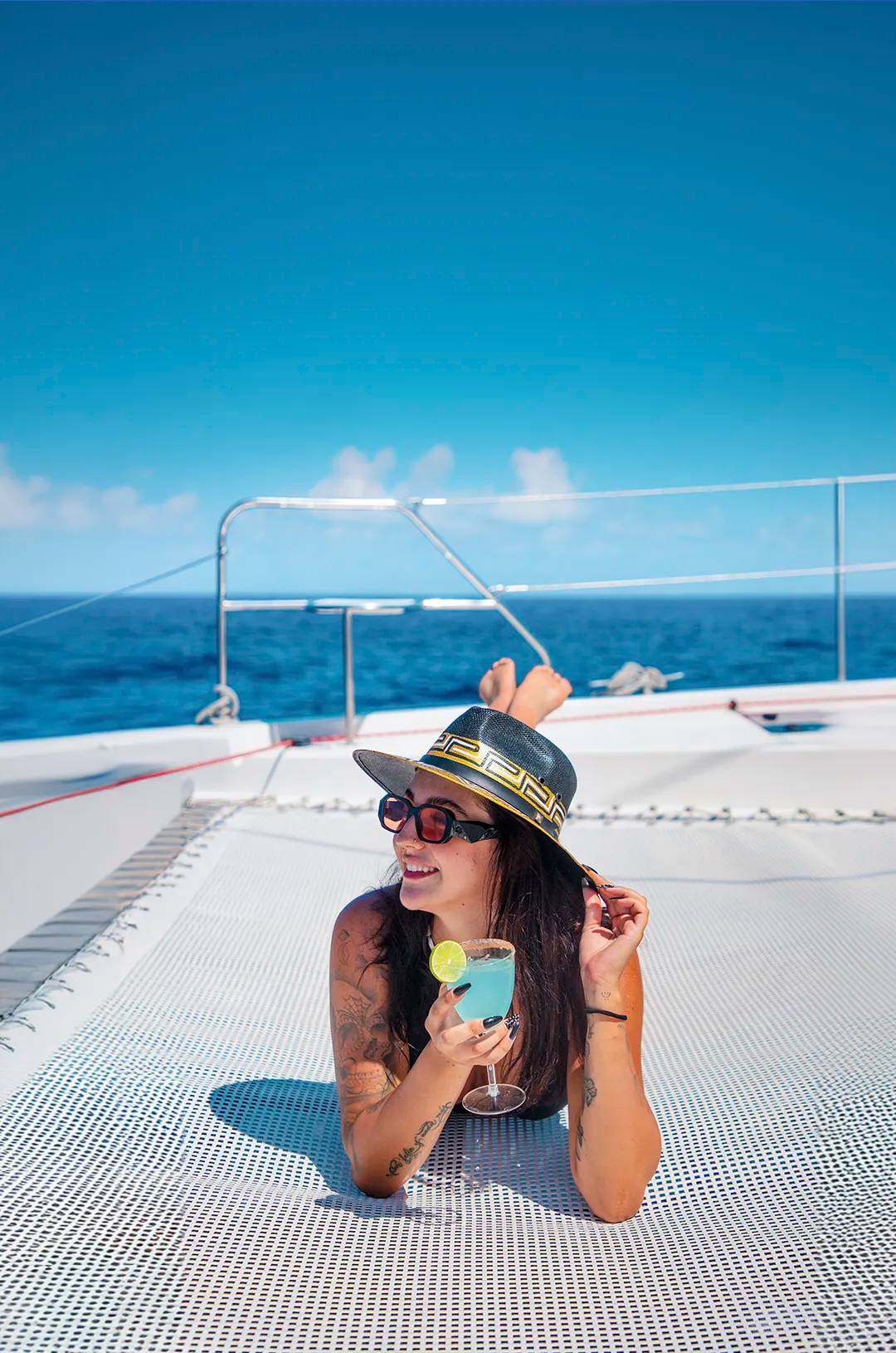 Girl sunbathing with a cocktail on board a Riviera Maya catamaran.