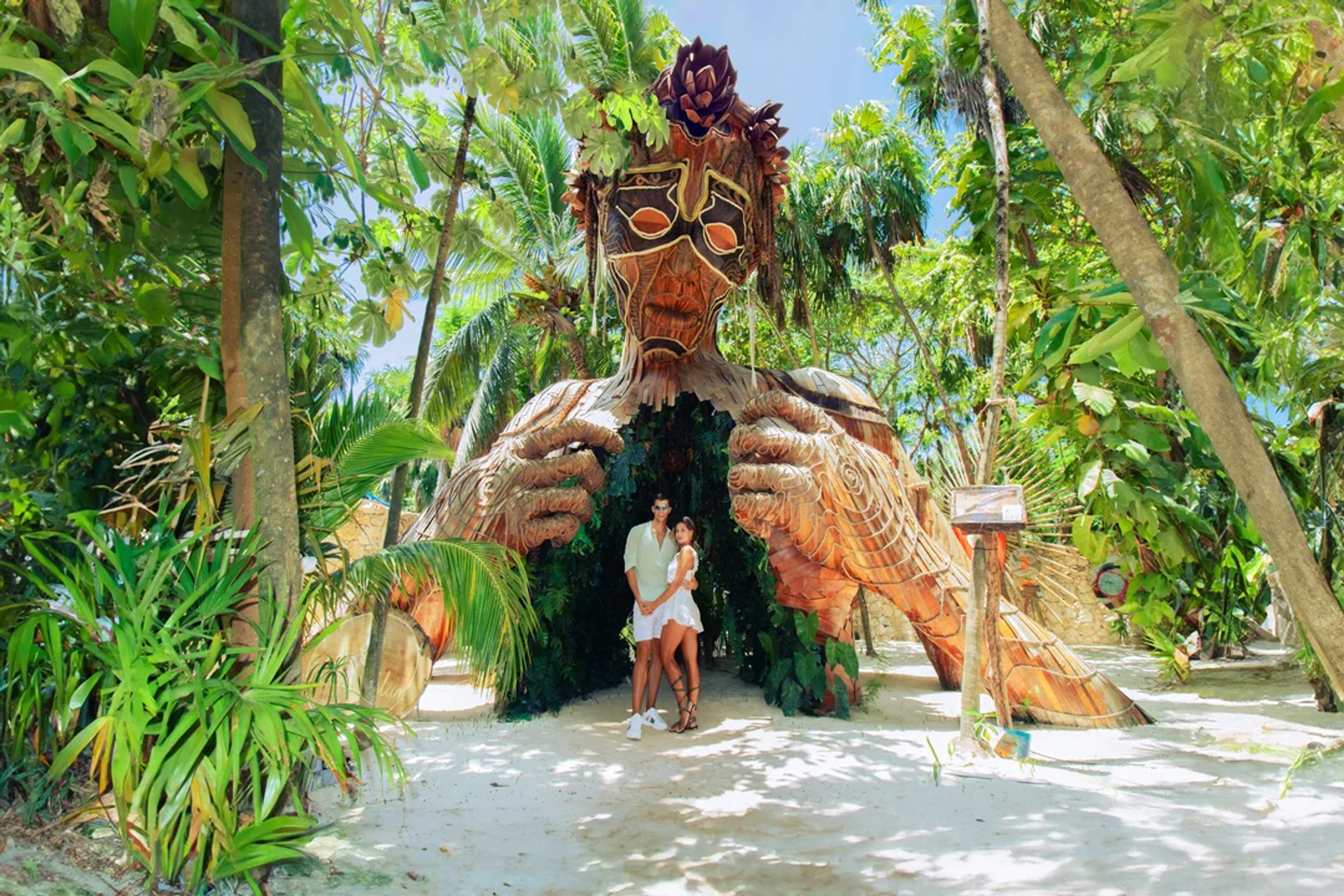 Couple poses beneath “Ven a la Luz,” a giant wooden sculpture surrounded by lush jungle in Tulum.