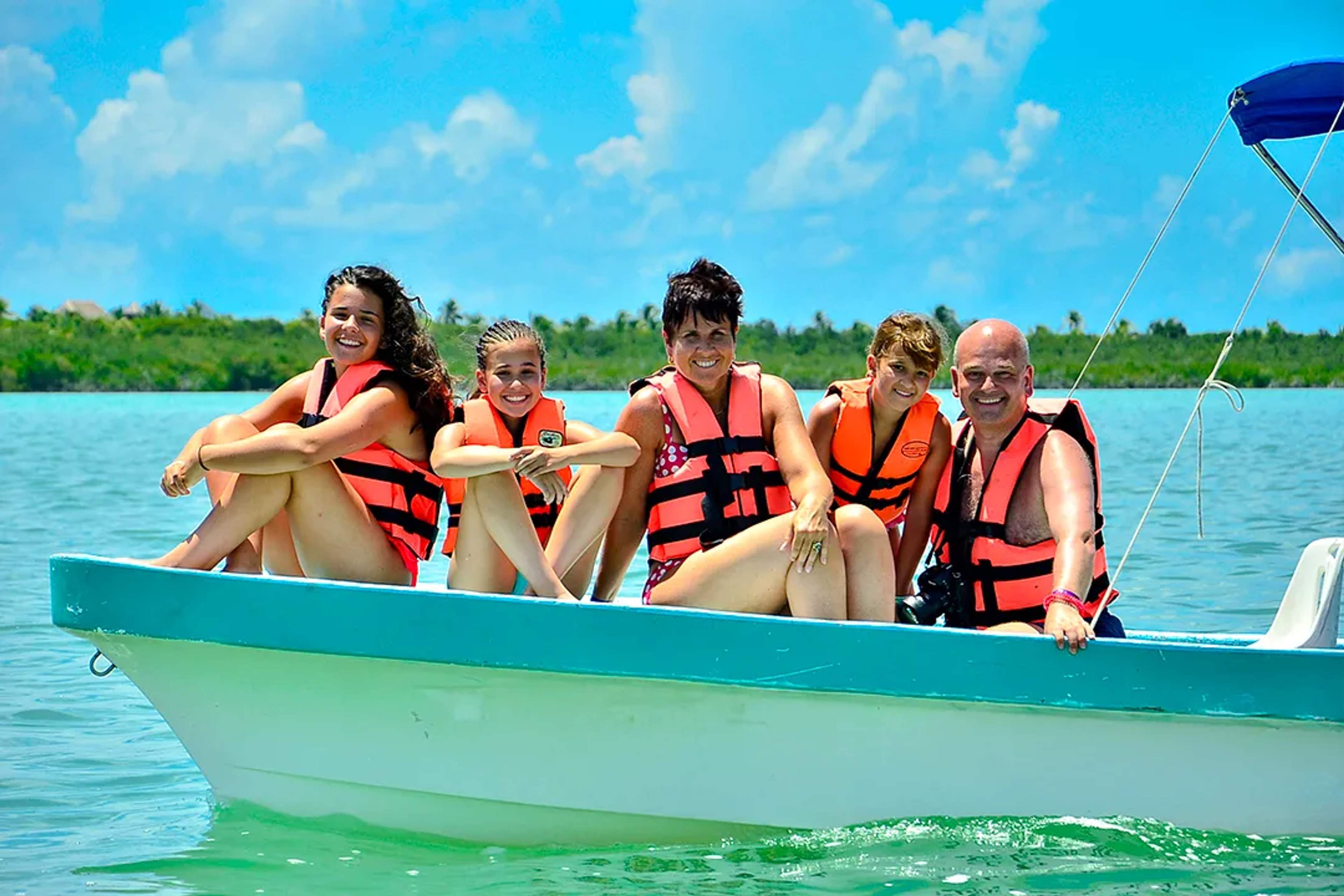 Family wearing life vests enjoying a boat ride on calm turquoise waters in Cancun, Mexico, during a tropical vacation