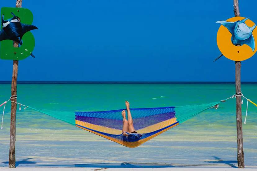 Person relaxing in a hammock on Holbox Island, with turquoise waters and clear blue sky.