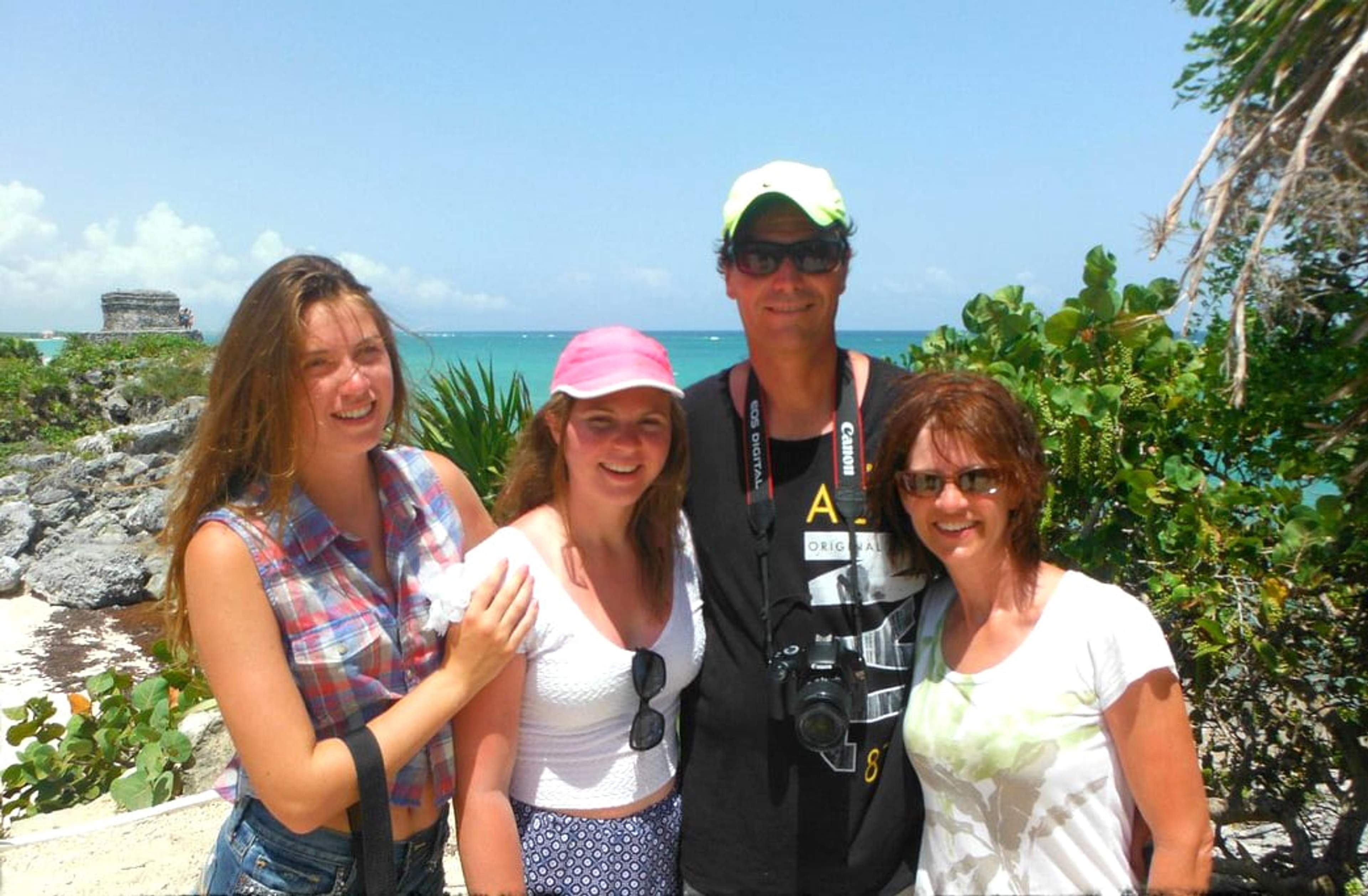 Familia posando frente a las ruinas de Tulum con el Mar Caribe de fondo en un día soleado.